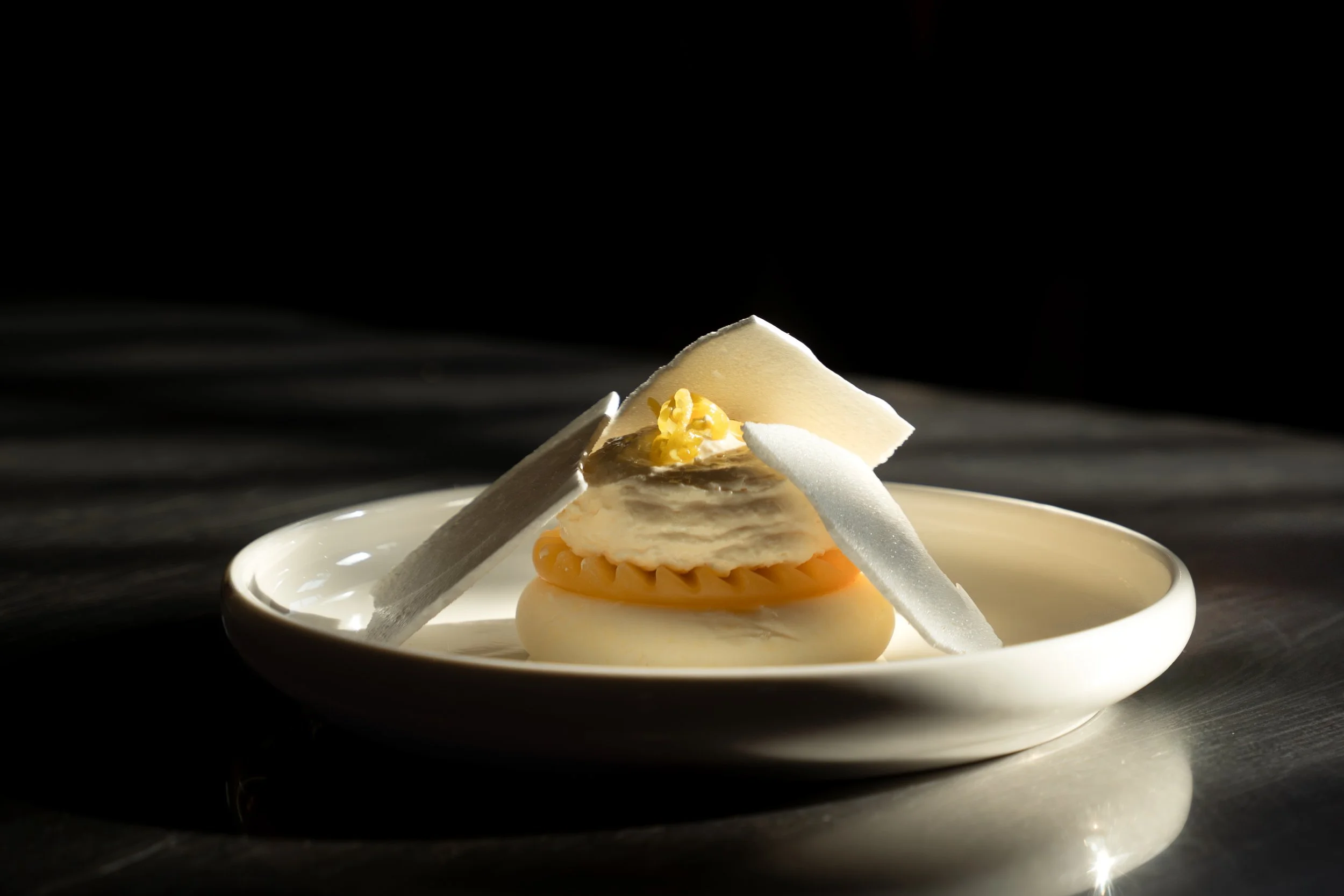 Een elegant wit bord met een delicat dessert bestaand uit lagen van witte chocolade, een stukje witte chocolade, en decoratief versierd met een kleine bloem of suiker decoratie.