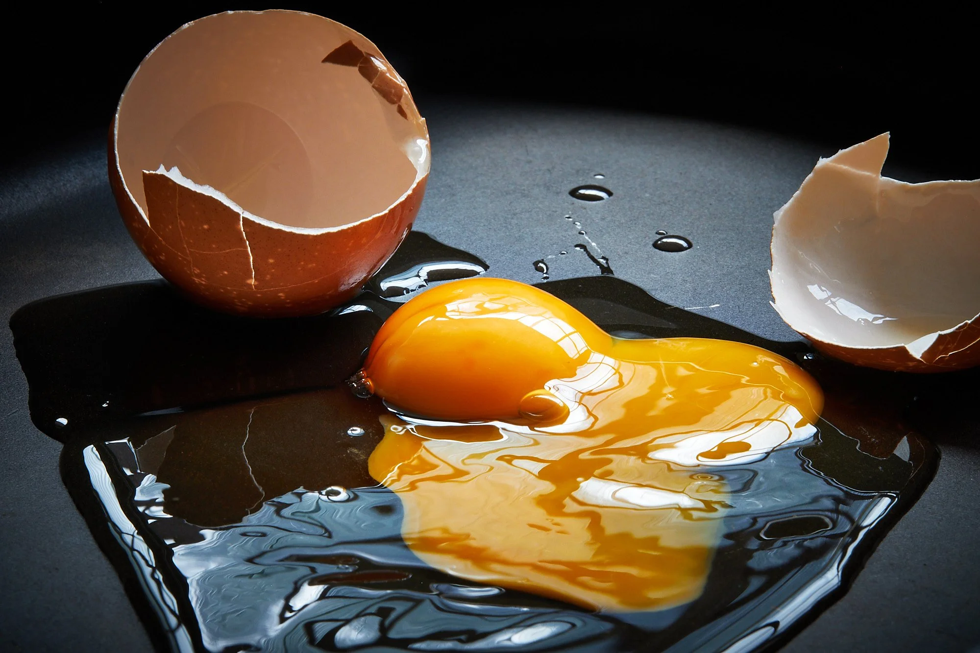 Broken eggshells with a raw egg yolk and spilled egg whites on a dark surface. Food photography in Sydney Australia.