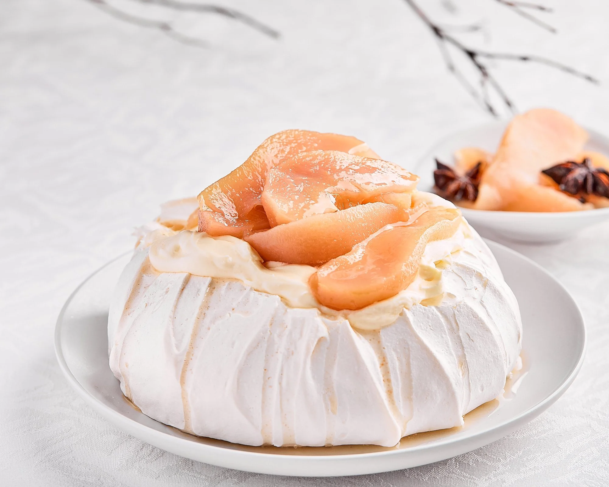 A pavlova dessert with a meringue base, topped with whipped cream and peach slices, served on a white plate. Dessert photo taken by Mah Vafaei in Sydney