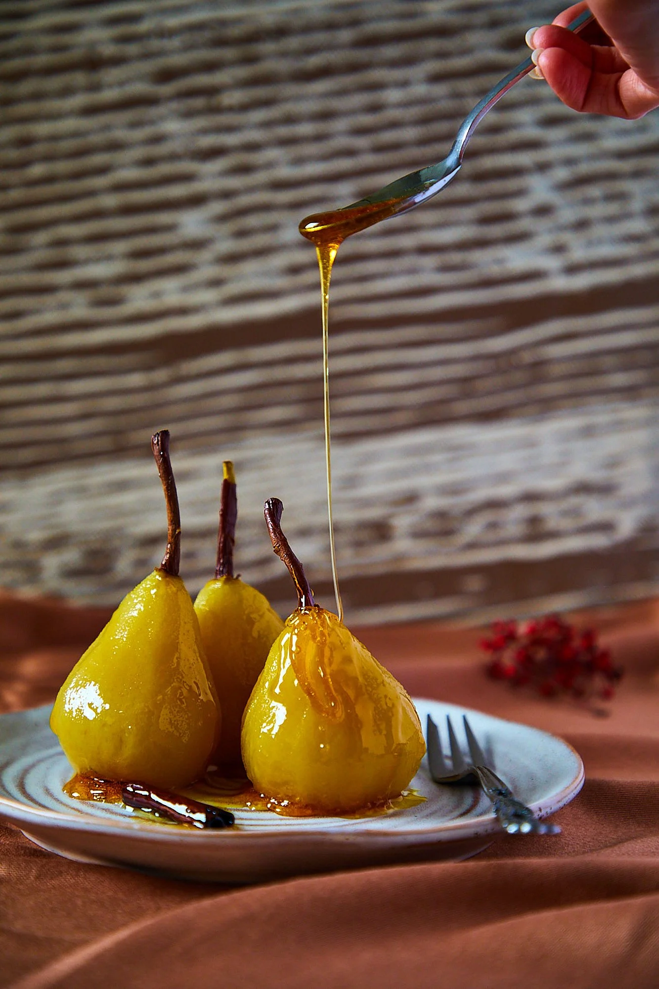 Three baked pears with caramel sauce on a white plate, with a fork and a hand pouring more caramel over the pears. Dessert photography, food photography, Sydney Australia.