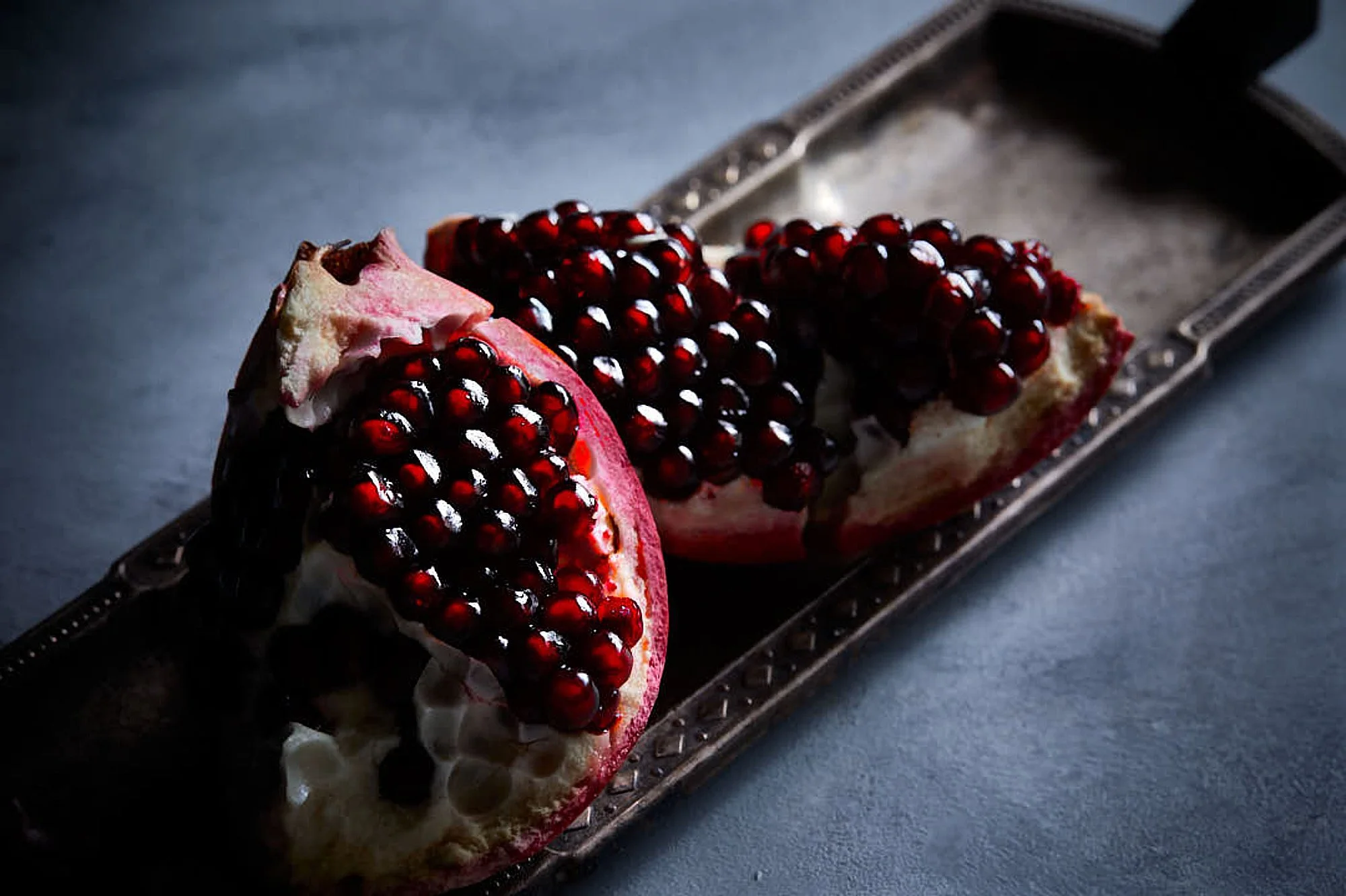 Pomegranate cut into quarters showing red seeds, on a metal tray. Fine art photography, commercial product photographer,Sydney