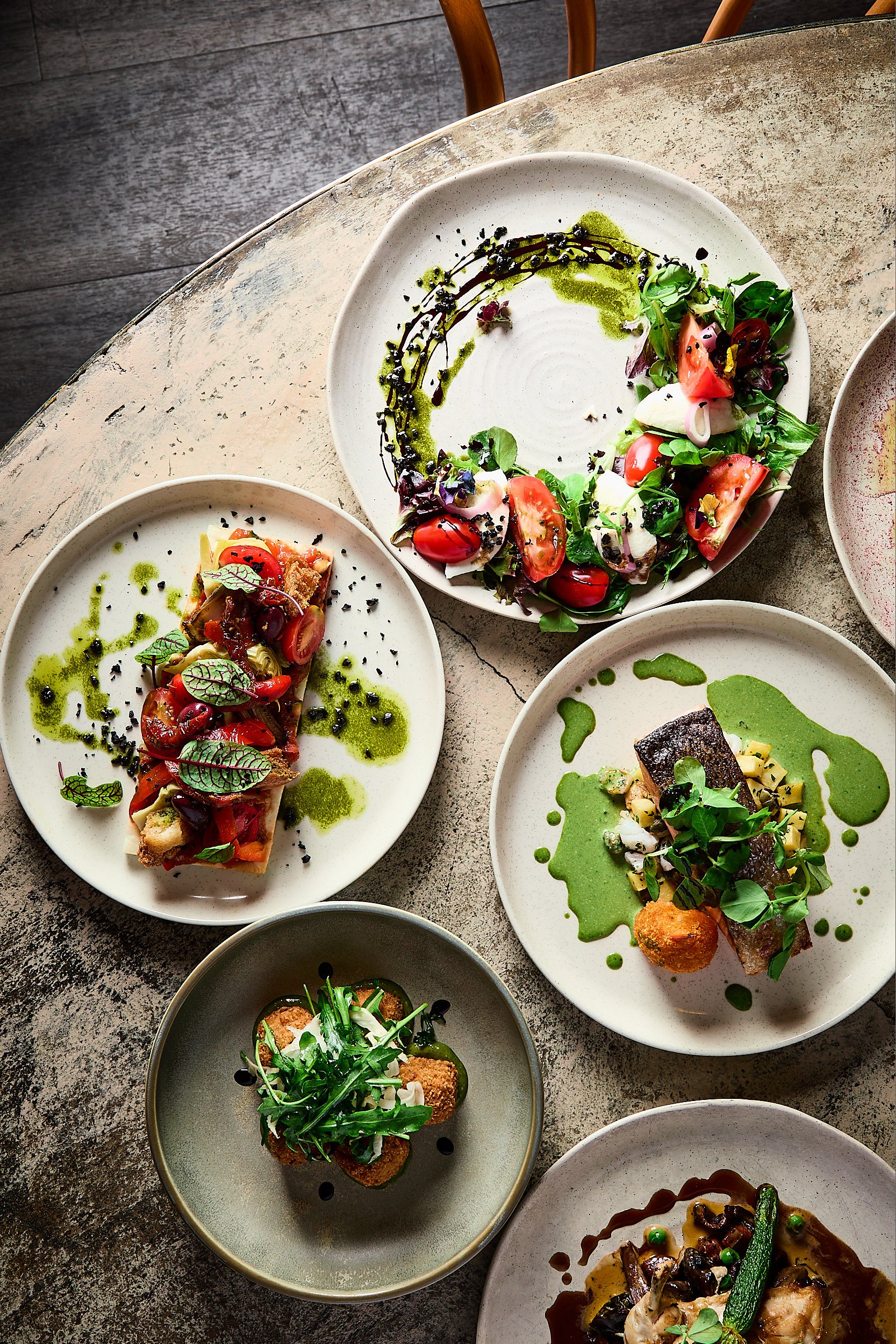 Assorted gourmet dishes on plates, including salads, appetizers, and entrees with garnishes and sauces, on a rustic table. Luxury restaurant photography in Sydney Australia. 