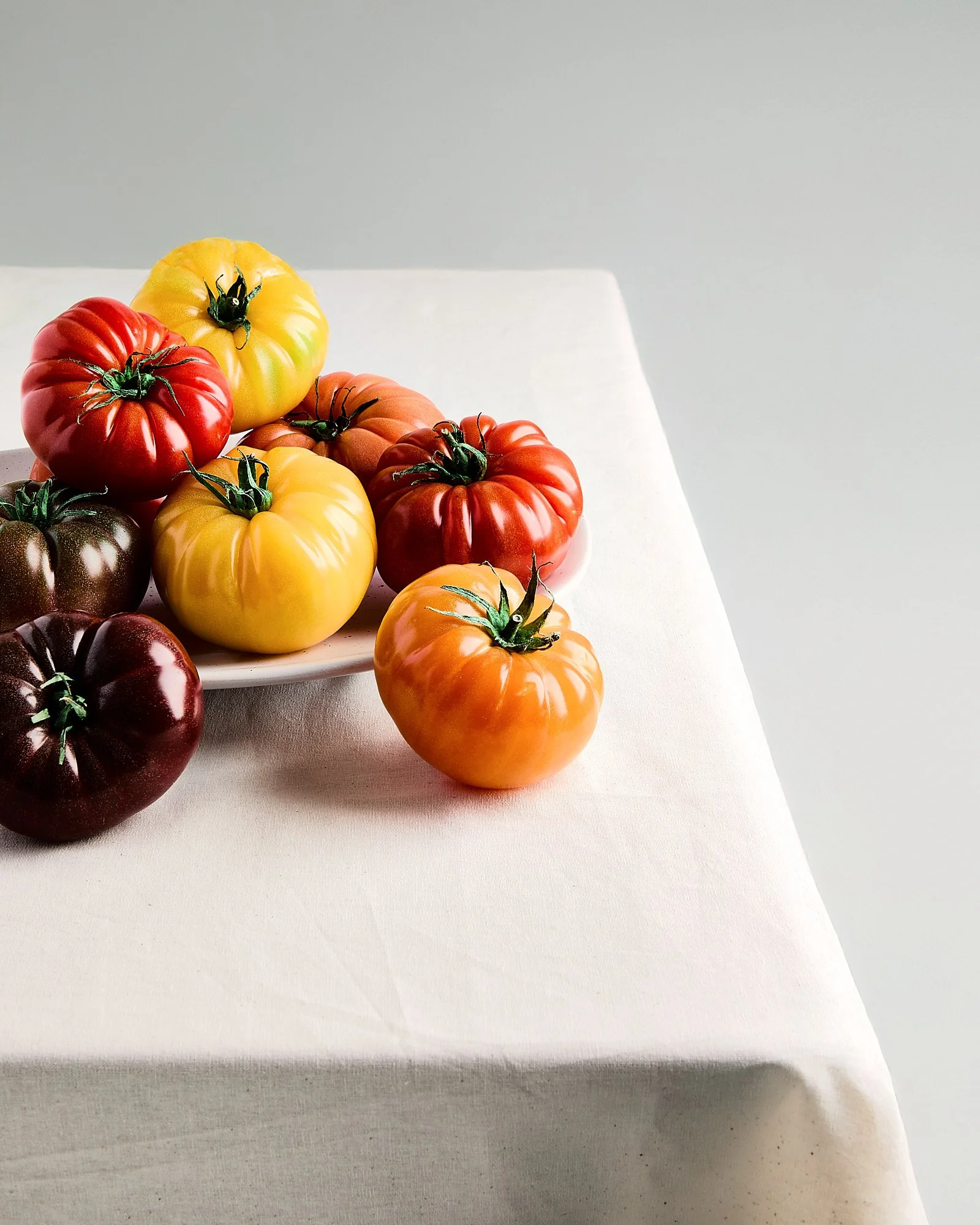 Colorful heirloom tomatoes in red, yellow, orange, and dark purple on a white plate and table. Fresh produce photography, Sydney photographer. 
