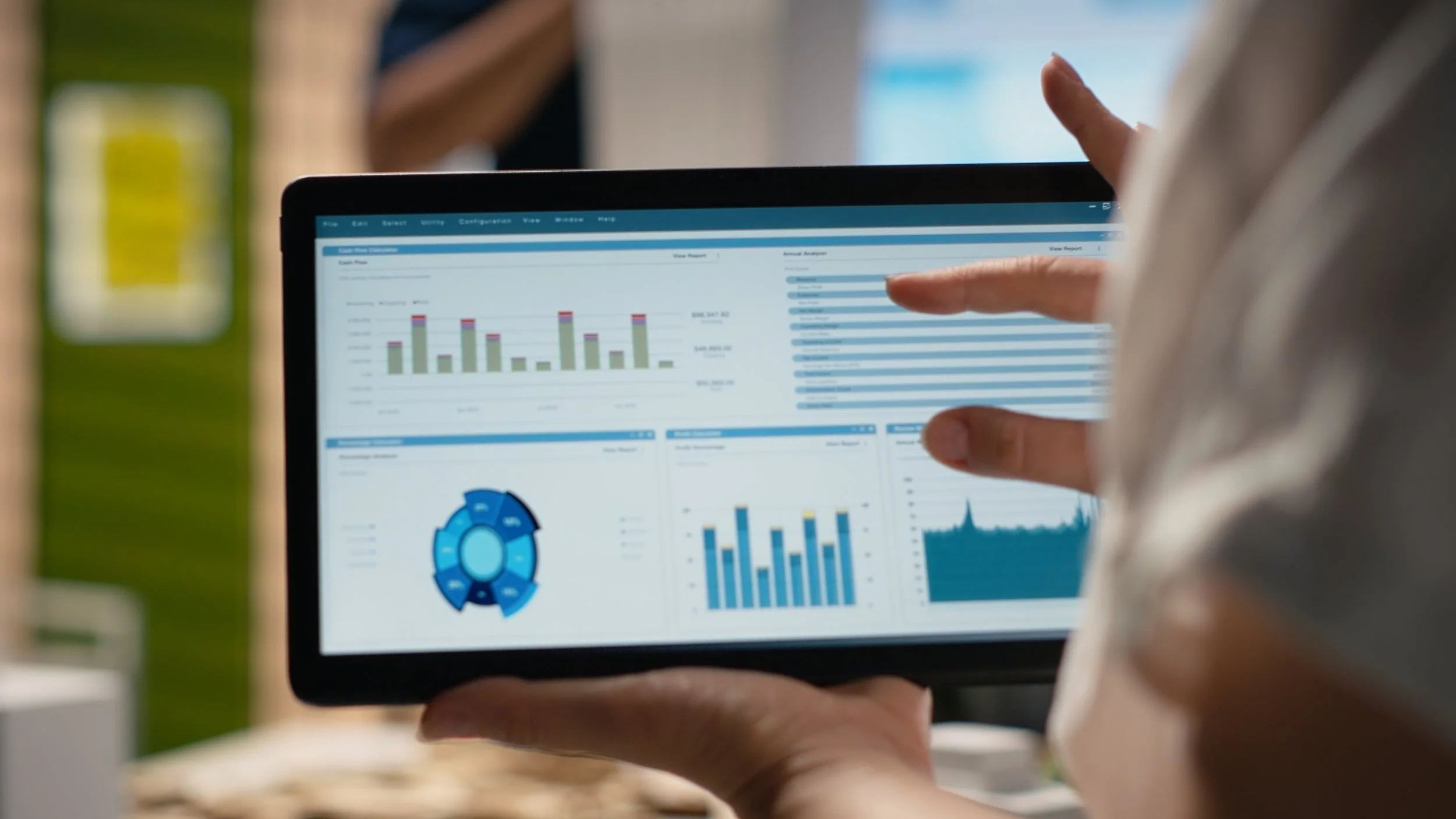 Person holding a tablet displaying various colorful charts and graphs with a person's hand pointing at the screen.