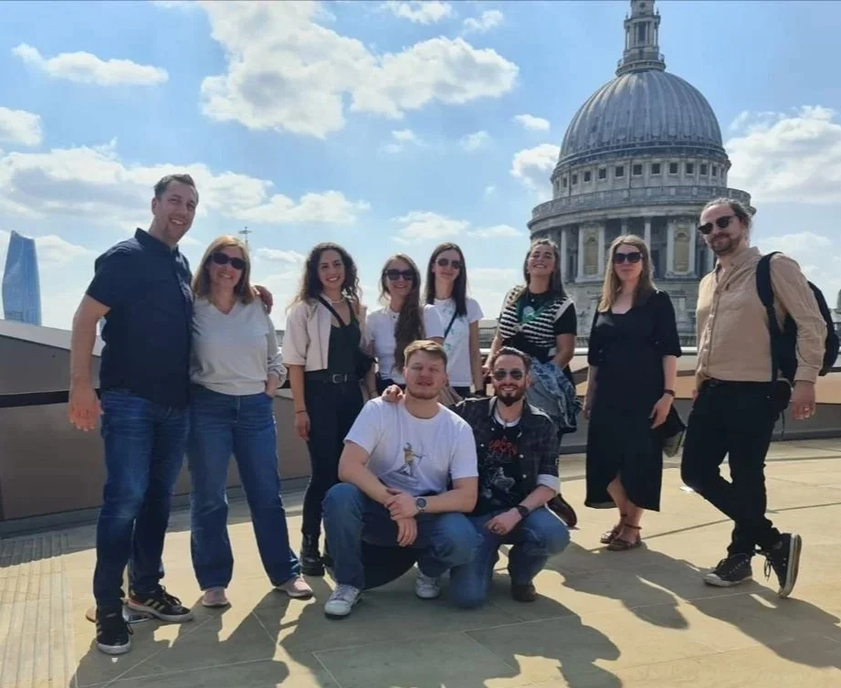 Group of nine people standing on a rooftop with St. Paul's Cathedral in London in the background, sunny sky with clouds.