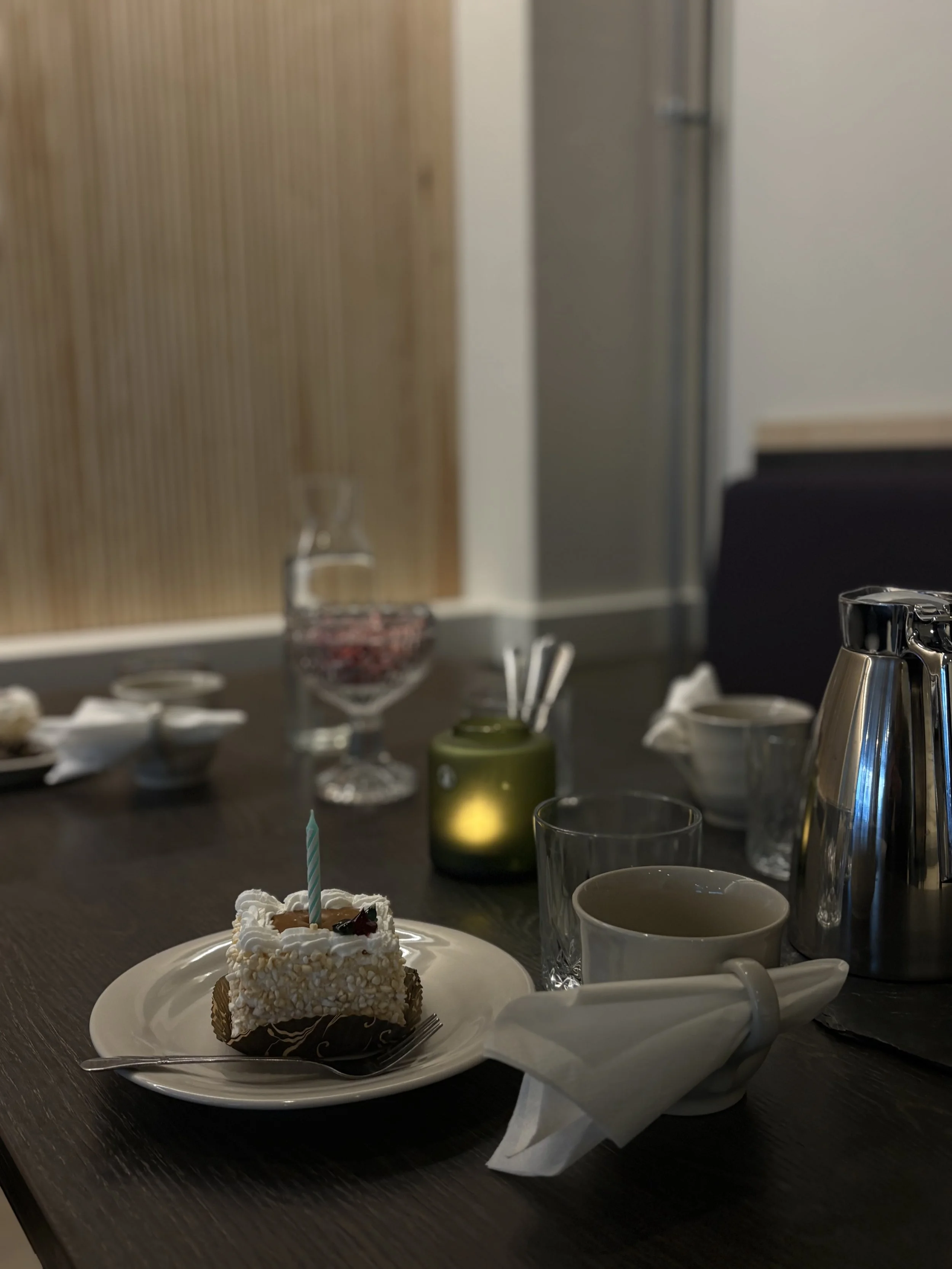 Syntymäpäiväkakku, jossa on sininen kynttilä, lautasella ja juomalaseja pöydällä