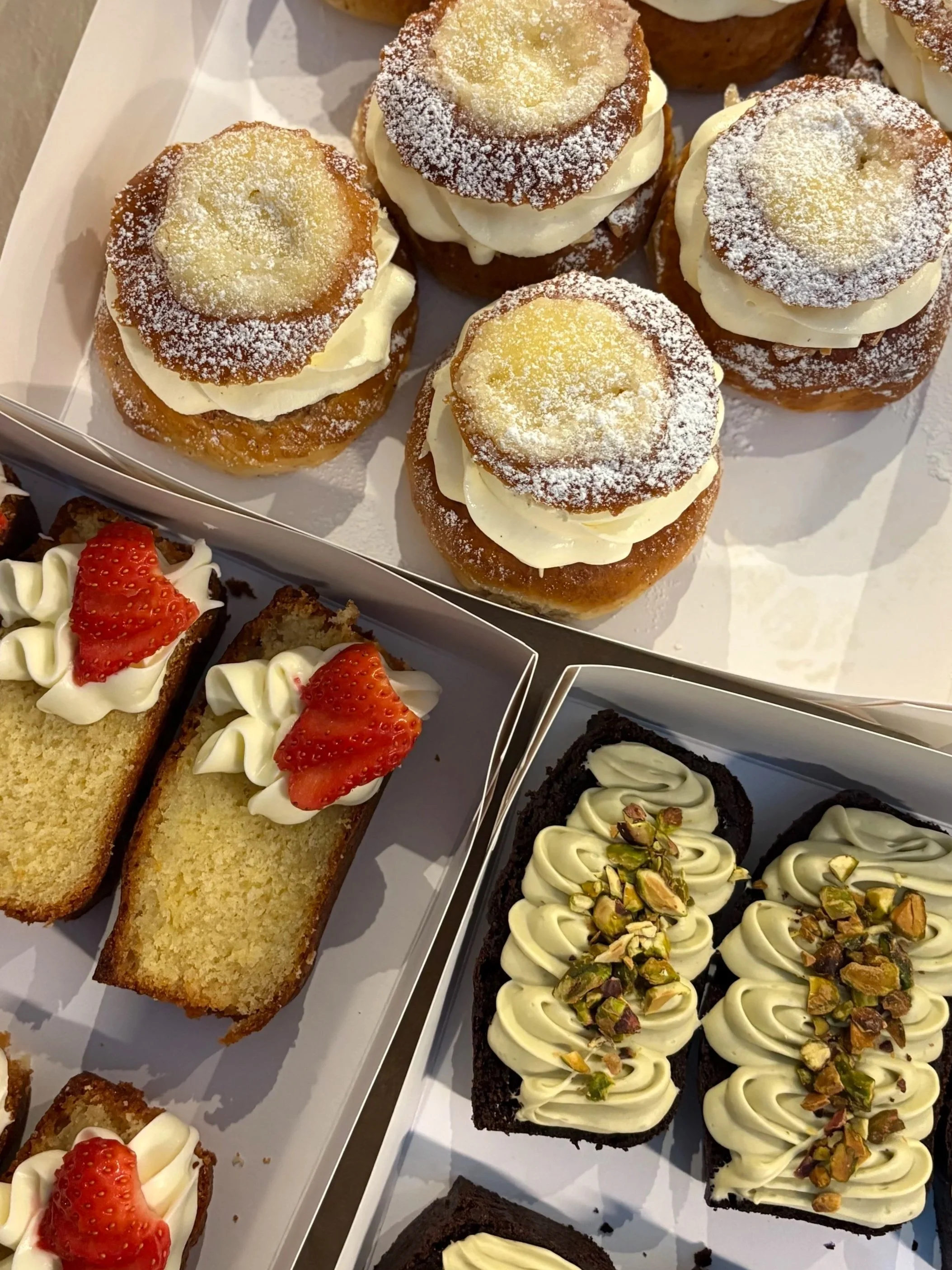 Eri tyyppisiä leivonnaisia, kuten sitruunapullia, kakkupaloja, joista osa on koristeltu mansikoilla ja pähkinöillä.