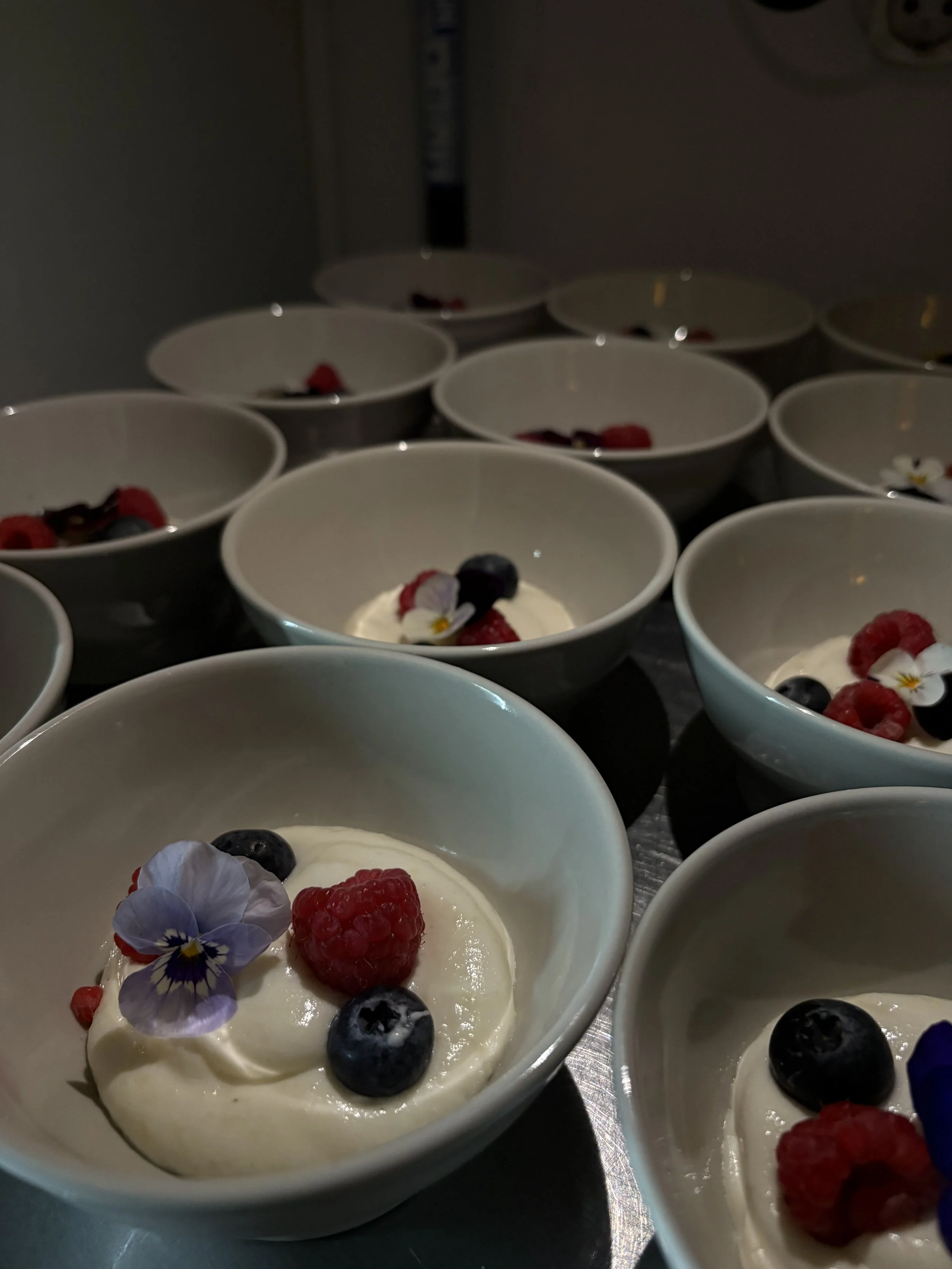 Kuvassa jälkiruokalautaset, jotka sisältävät jogurttia, marjoja ja kukkamaisia koristeita.