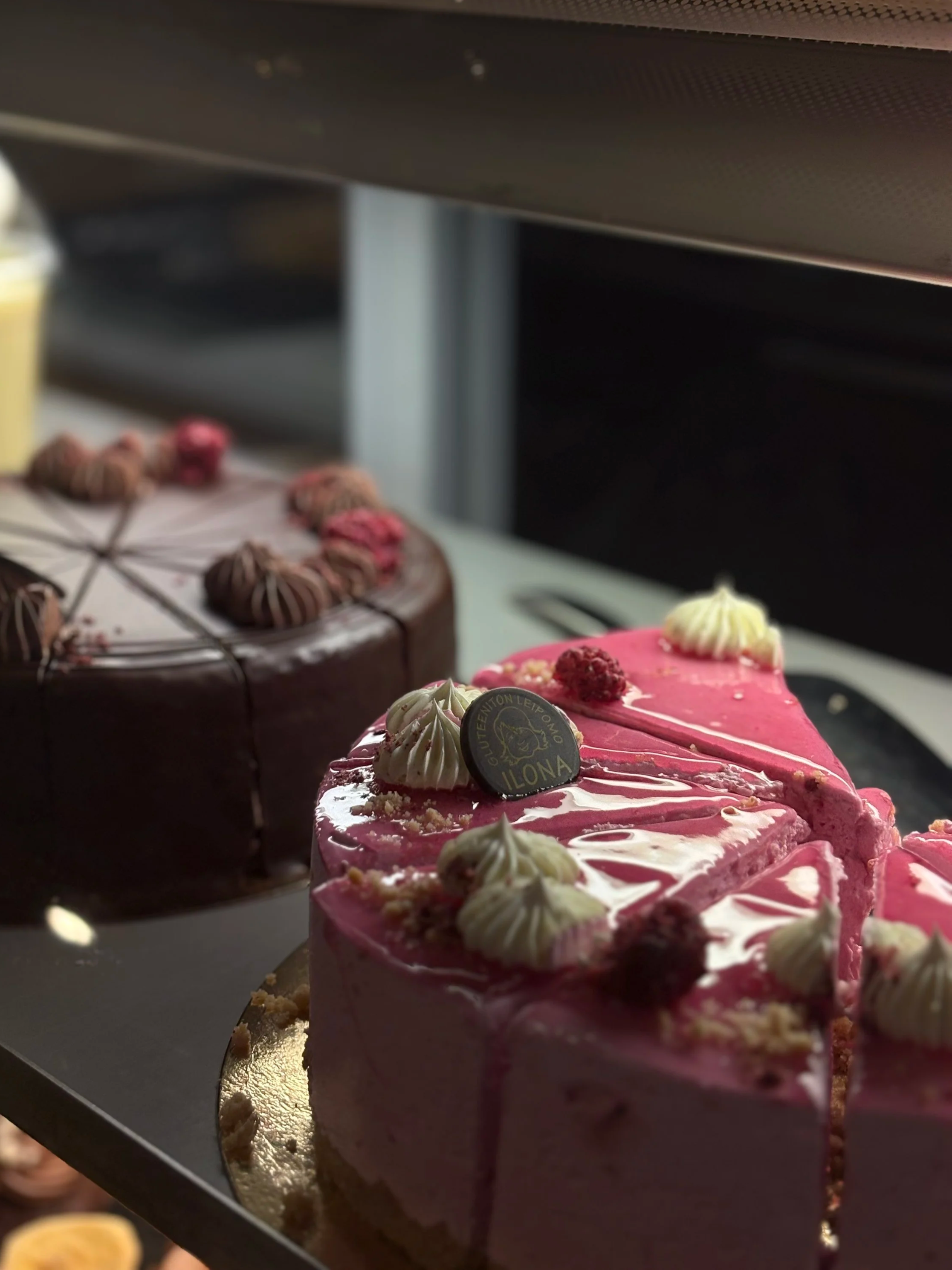 Kaksi juustokakkua, yksi vaaleanpunainen ja toinen suklaa, esillä vitriinissä.