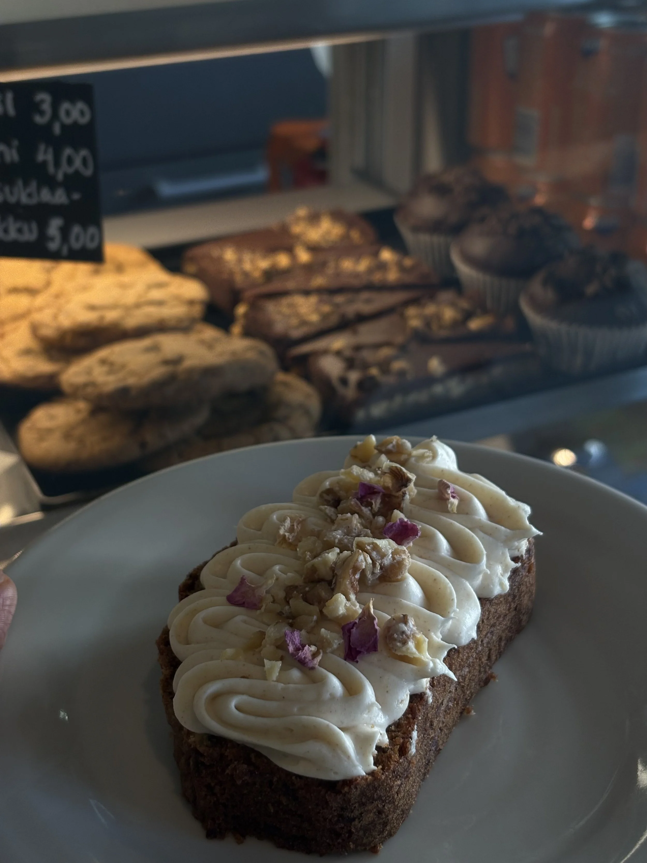 Tuore kakkupala päällystettynä, taustalla leivonnaisia JAM Café & Barin leipomomyymälässä.