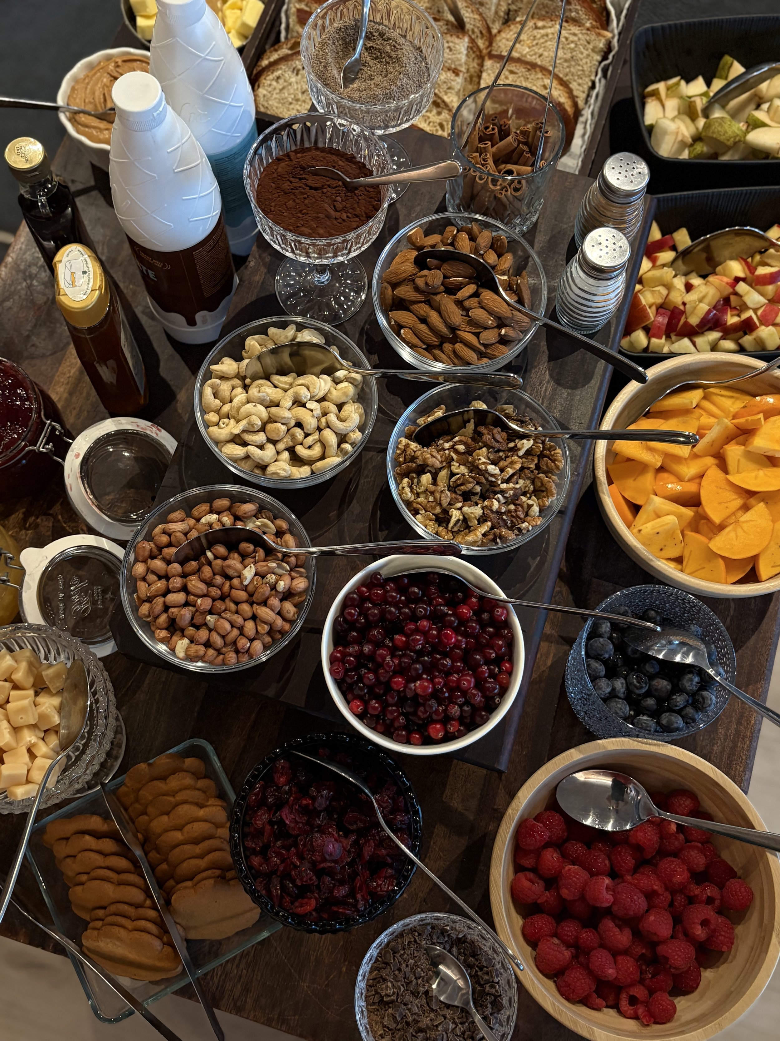 Riisipuurobuffet joulun aikaan, jossa on erilaisia marjoja, pähkinöitä, suklaata, leipiä, maitoa, hunajaa ja hedelmiä.