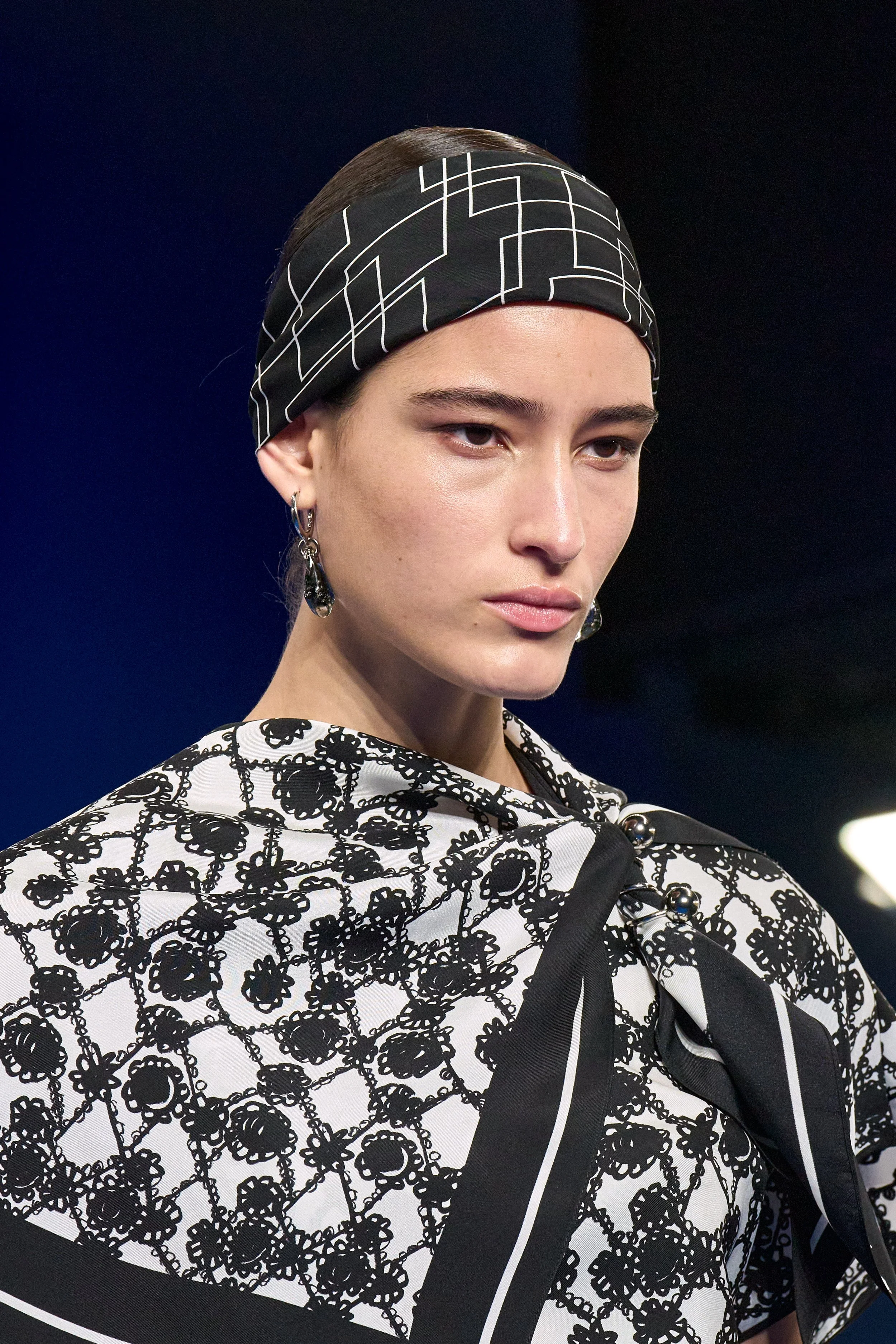 Mode-Modenschau mit einer jungen Frau, die einen schwarz-weißen Haarschal und ein passendes Outfit mit floralem Muster trägt.