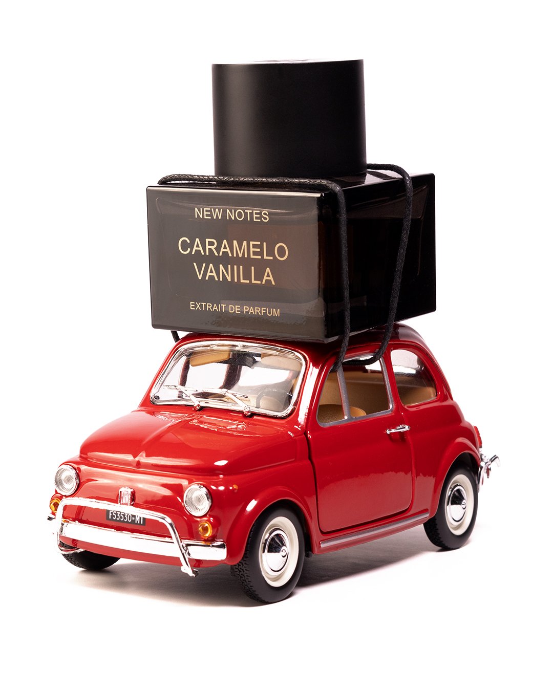 Ein rotes Spielzeugauto mit einem schwarzen Parfümflakon auf dem Dach, der mit einem schwarzen Y-strap befestigt ist.