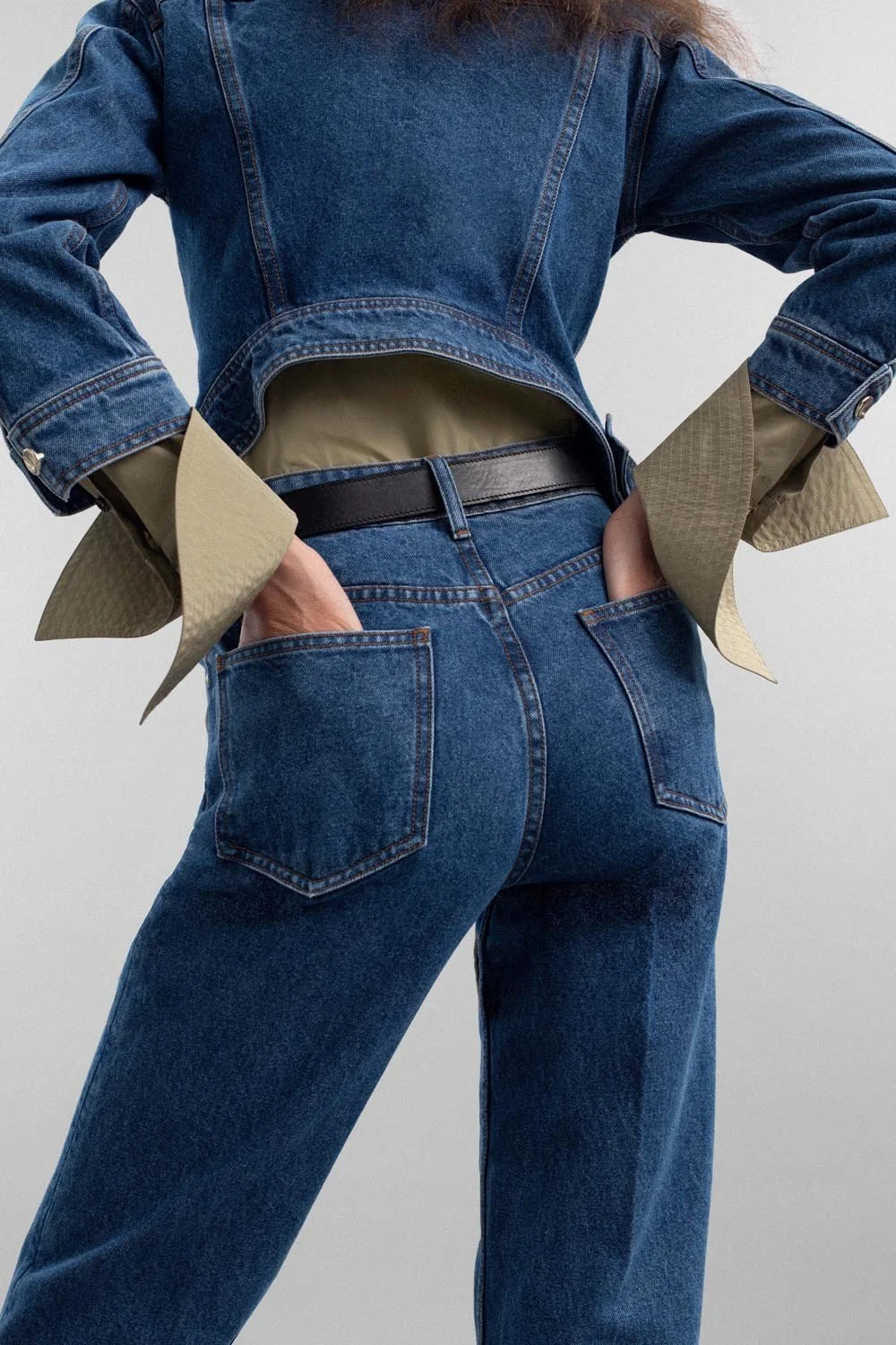 Eine Person trägt eine Jeansjacke, eine Jeanshose, einen schwarzen Gürtel und eine beige Schicht unter der Jacke.