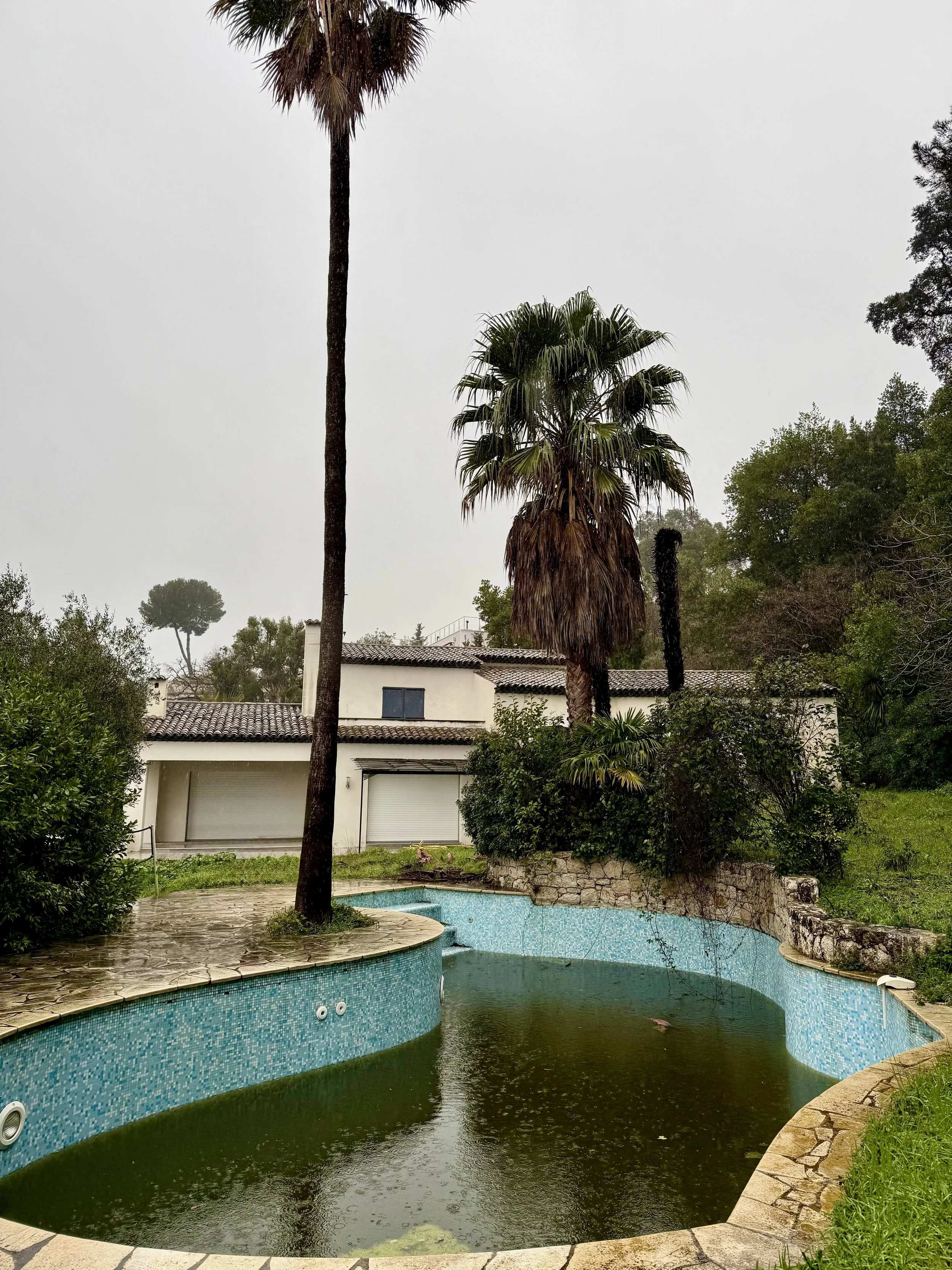 Escalier avec rampe en métal noir et or, murs en pierre claire, grandes fenêtres à cadre rouge laissant passer la lumière naturelle.
