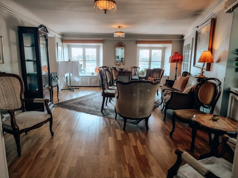 Living room with vintage furniture, hardwood floors, large windows, and soft lighting.