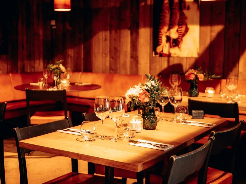 Restaurant table set with glasses, silverware, candles, and floral centerpieces in a cozy, warmly-lit dining area