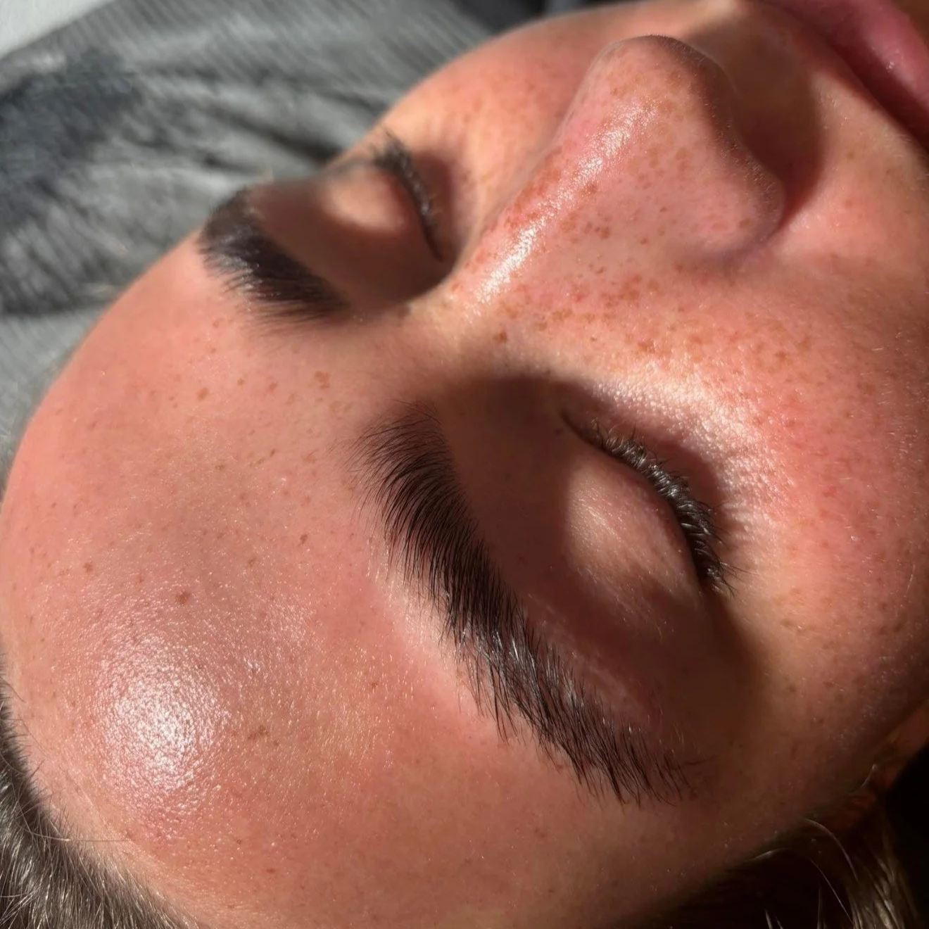 Close-up of a woman's face with closed eyes, showing freckles and smooth skin, lying down.