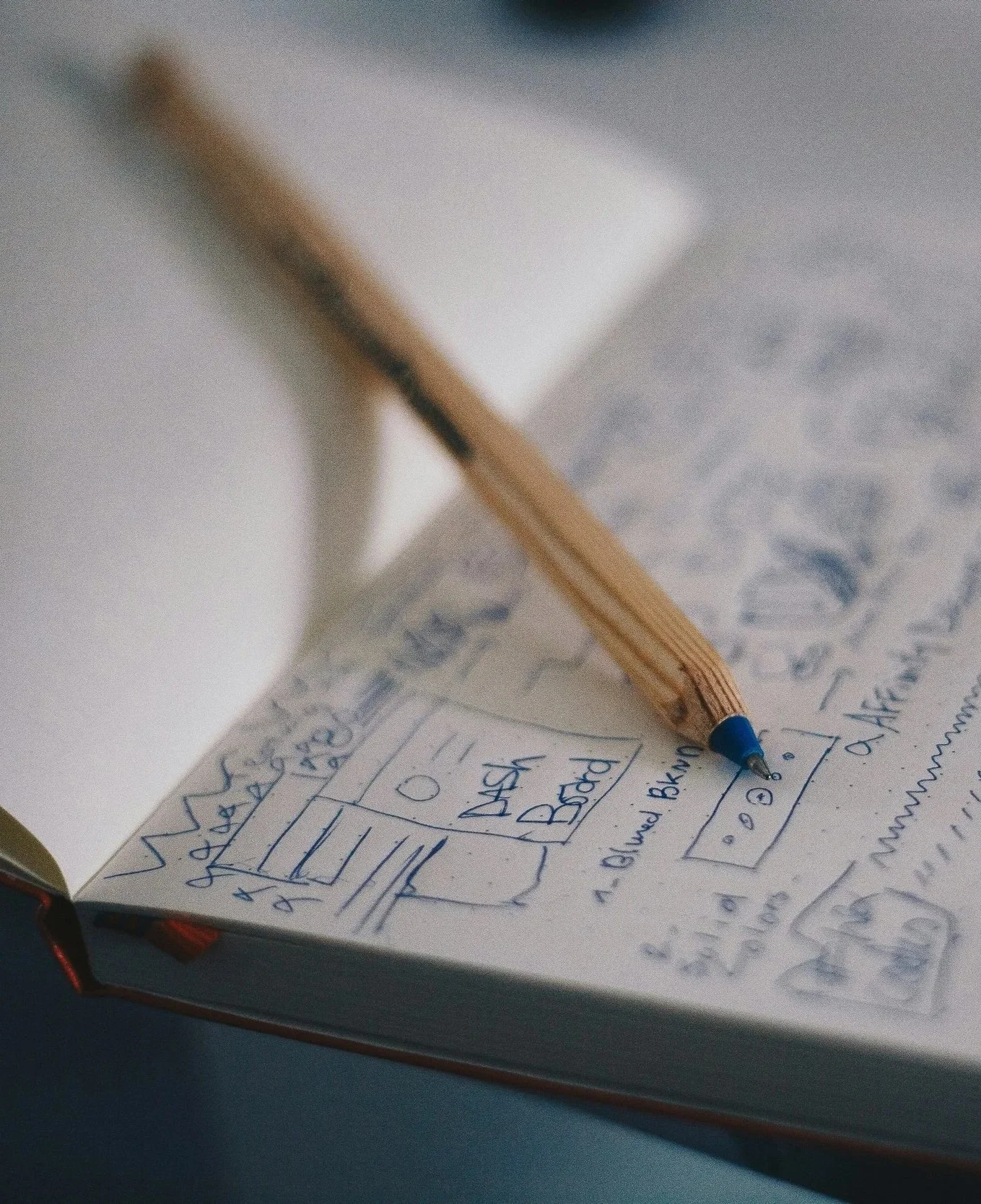 A notebook with handwritten sketches and notes, a cardboard box drawn with boxes labeled 'Dash' and 'Bath,' and a wooden pencil resting on the page.