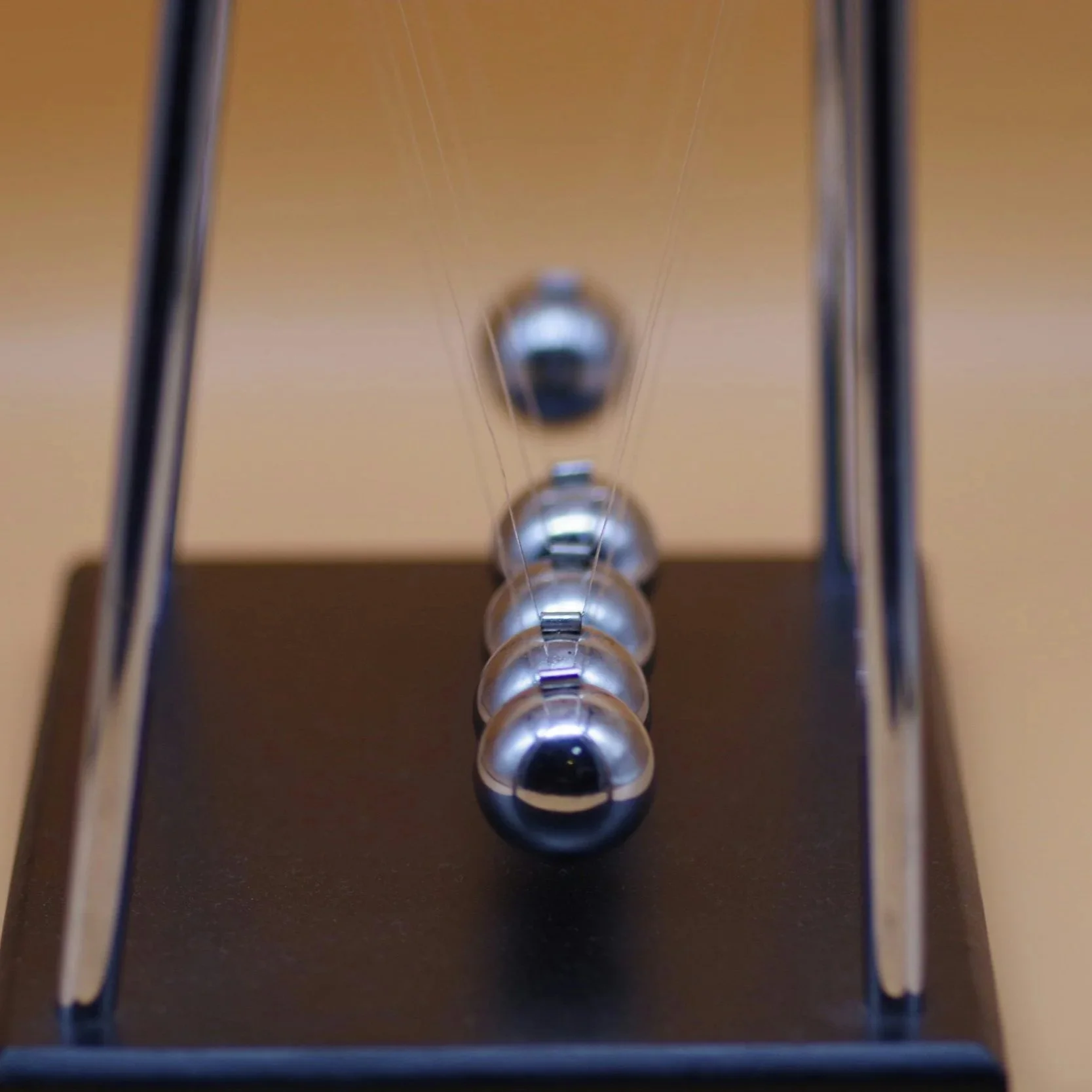 Close-up of a Newton's cradle with five metallic spheres suspended by thin wires inside a rectangular frame.