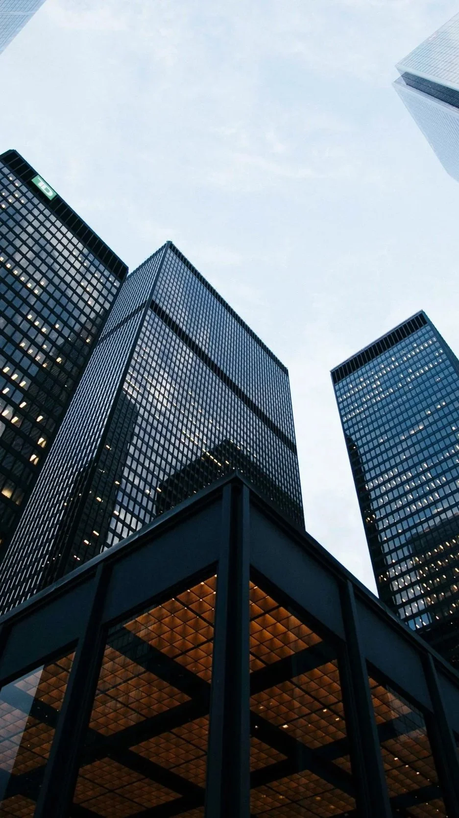 A low-angle view of tall modern office buildings with glass facades in an urban cityscape during dusk.