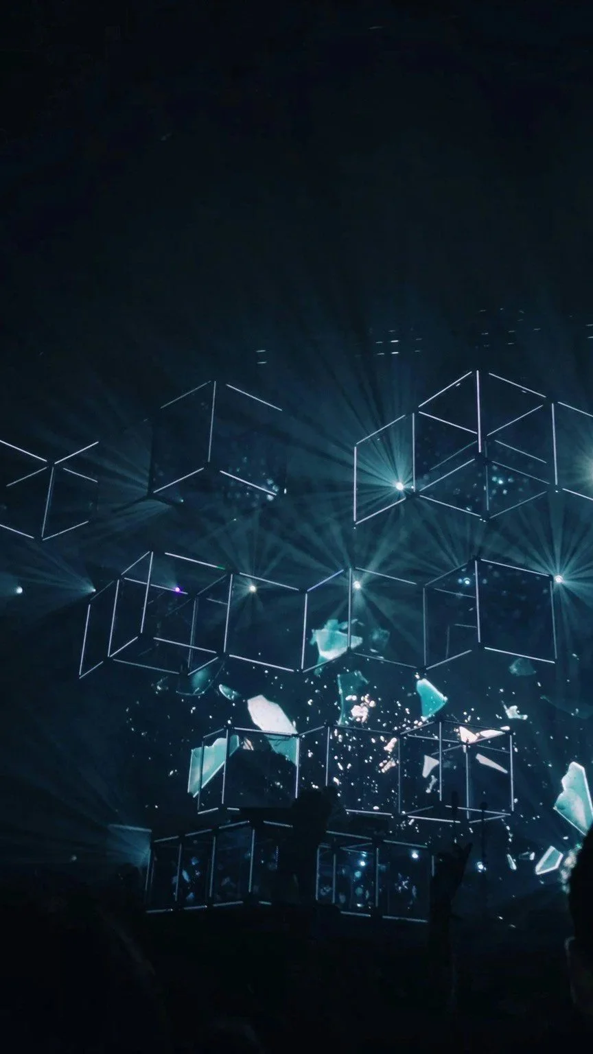 A digital or virtual scene with geometric light structures, possibly cubes, arranged in a 3D formation, with glowing effects and particle effects creating a futuristic, high-tech atmosphere.