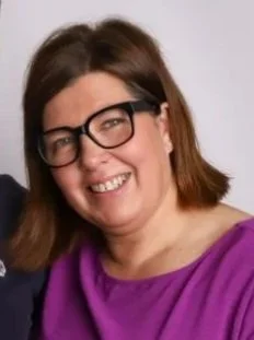 A woman with brown hair, glasses, and a purple top smiling at the camera.