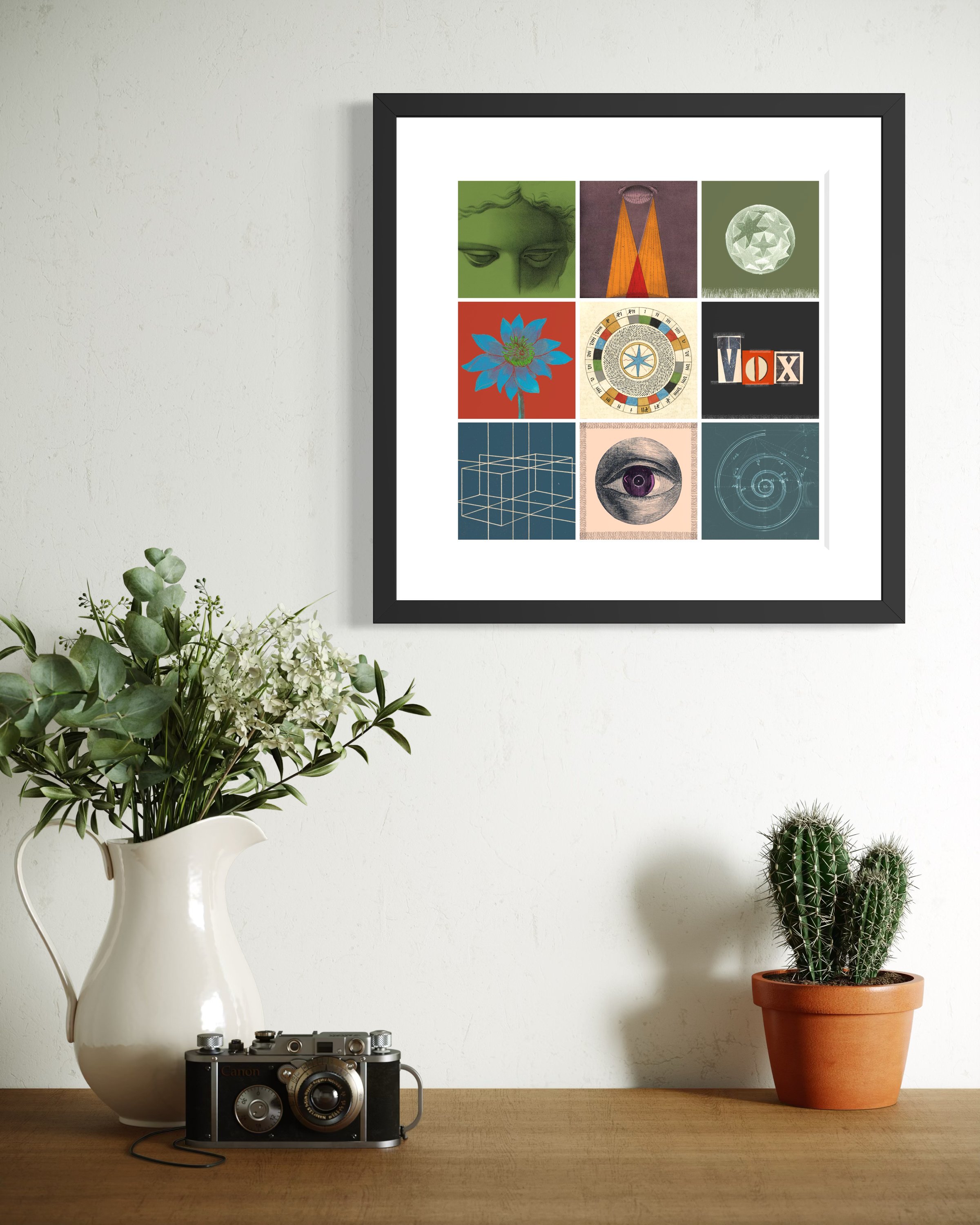 Alchemy fine-art print in a black gallery frame displayed on a wall above a wooden surface with a vintage camera, a white jug of flowers and a potted cactus