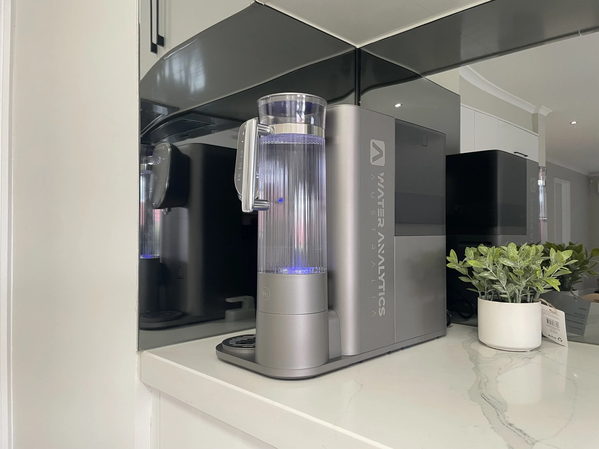 A water purifier machine on a kitchen counter with a potted plant beside it.
