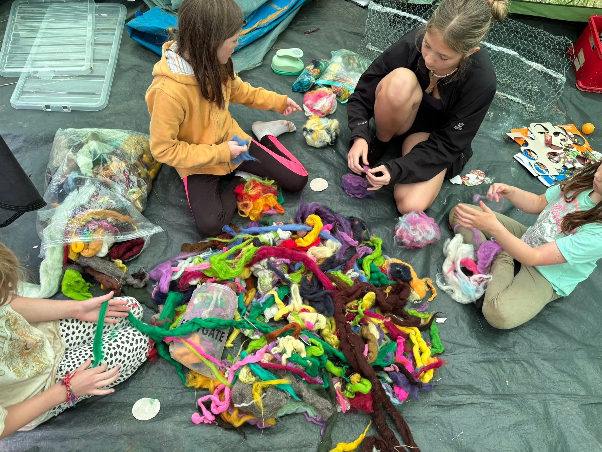 Children sitting on a tarp sorting and making arts and crafts with colorful yarns and fiber.