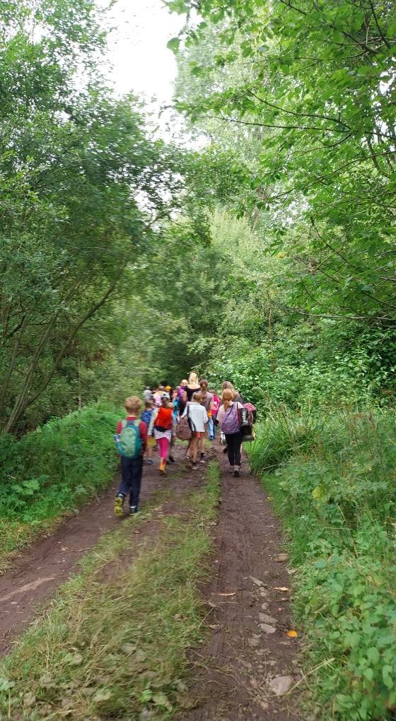 A group of children and adults walking along a dirt trail in a lush, green forest.