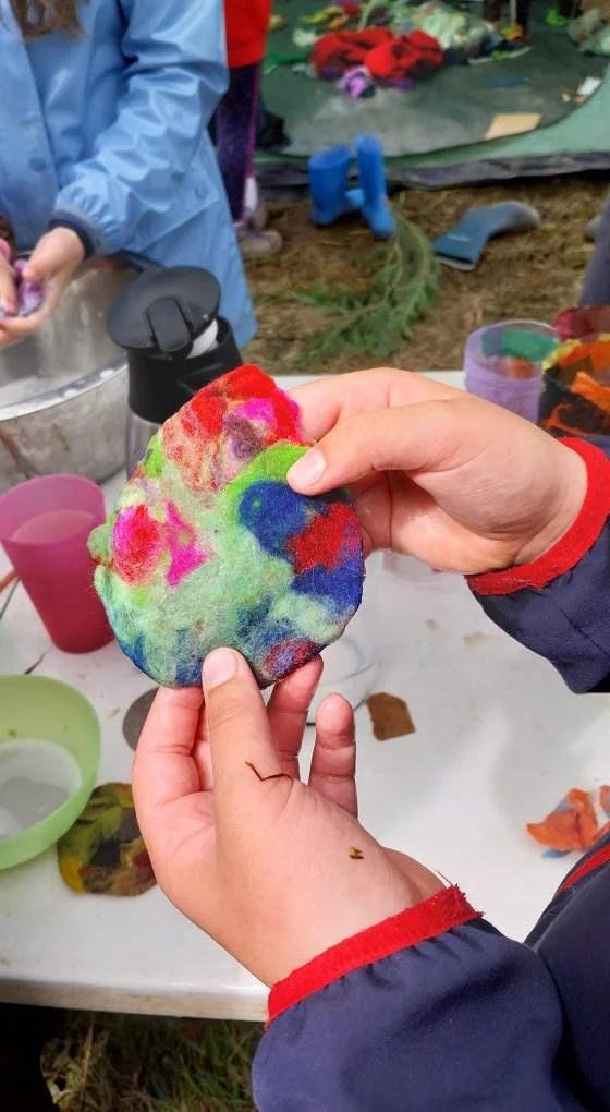 Person holding a colorful felted rock with tie-dye pattern during an outdoor craft activity.