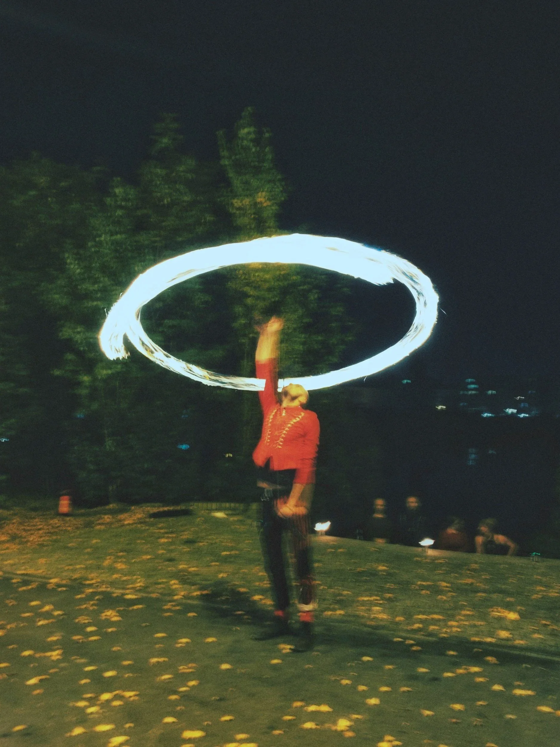 Person in red jacket performing a fire spinning trick creating a large circle of fire in the air at night outdoors.