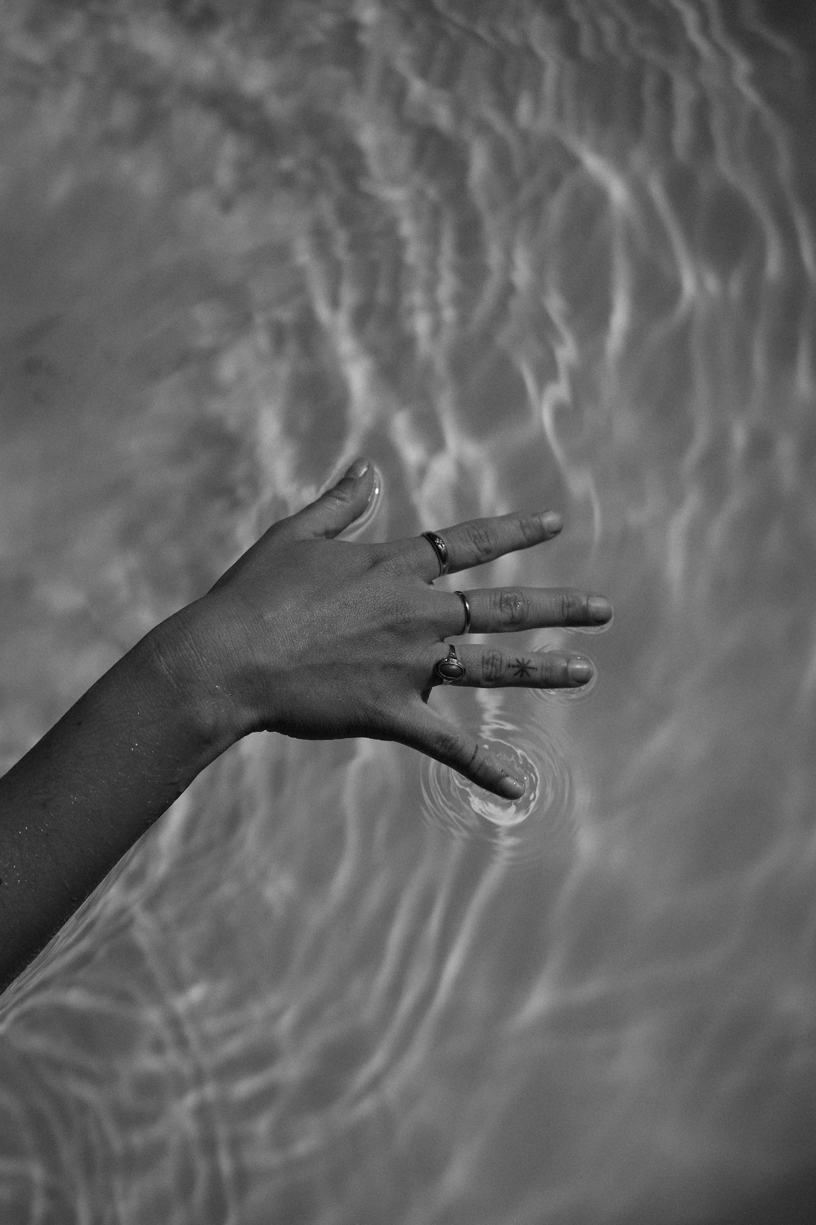 A hand with rings reaching into water, creating ripples.