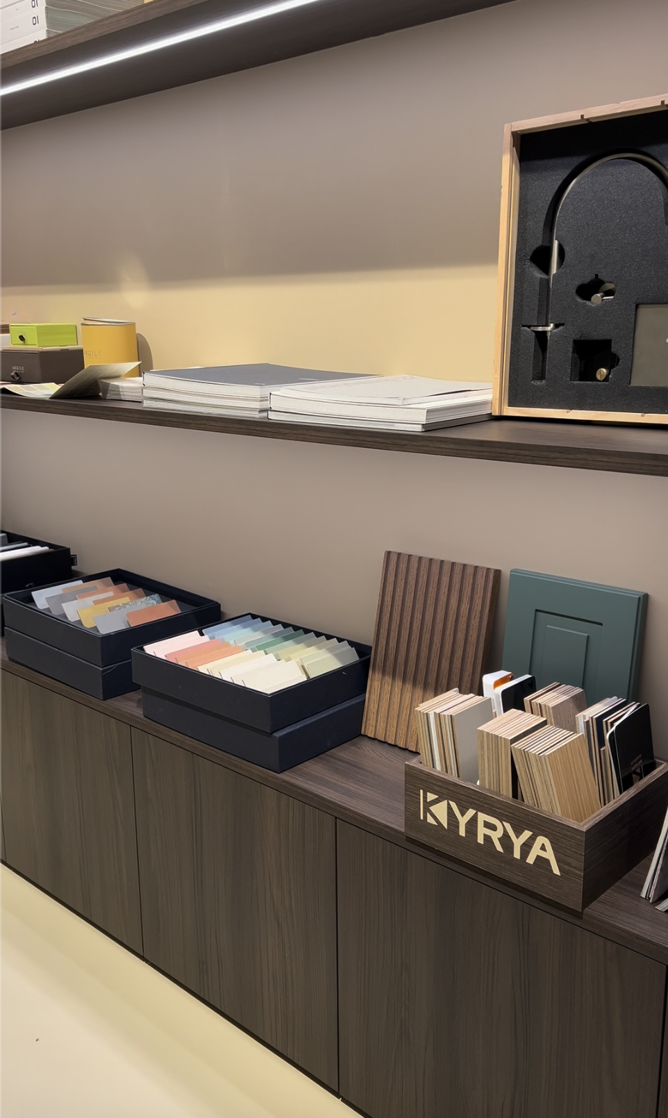 Exposition de matériaux de décoration pour la maison, comprenant des échantillons de couleurs, de textures et de matériaux dans des boîtes, avec des échantillons en bois, en métal et en plastique.