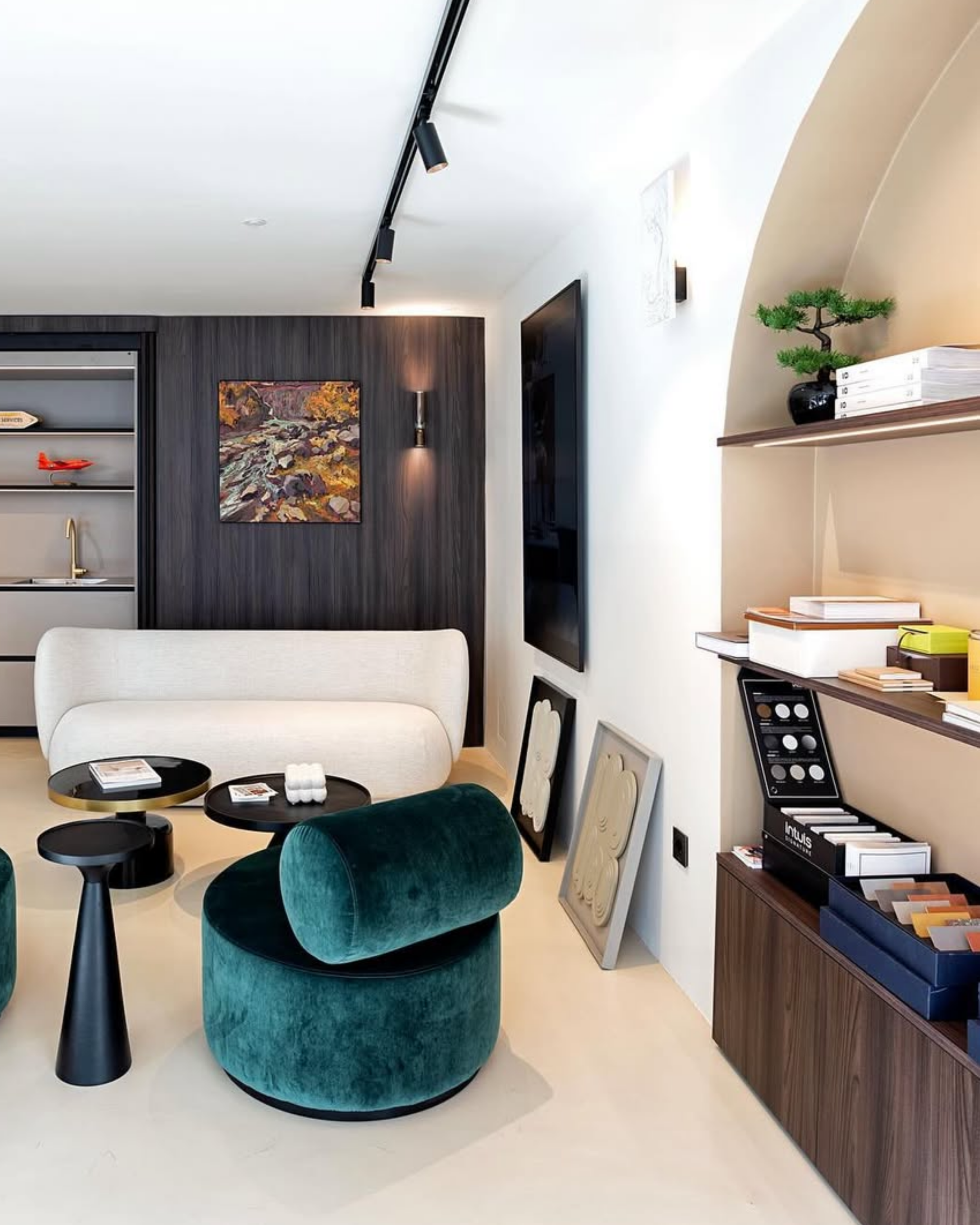 Salon moderne avec canapé blanc, fauteuil vert foncé, tables basses noires, étagères en bois avec livres, peinture murale, décoration minimaliste, éclairage encastré, écran plat sur le mur, œuvres d'art éclaboussées.