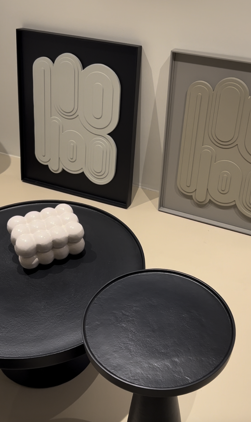 Deux cadres avec des motifs graphiques en relief, une sculpture blanche en forme de boule, et deux tables noires Rondes
