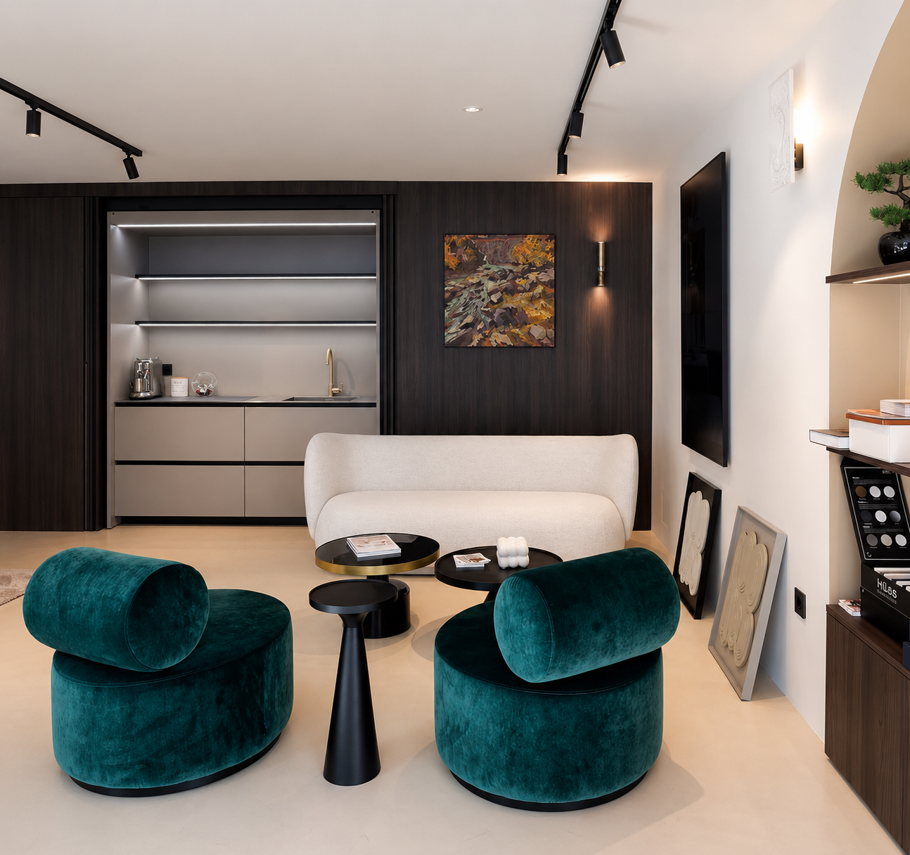 Salle de séjour avec deux fauteuils en velours vert, un canapé beige, tables basses noires, mur en bois foncé avec une peinture abstraite, petite cuisine en arrière-plan, étagères décoratives et tableau sur le sol.