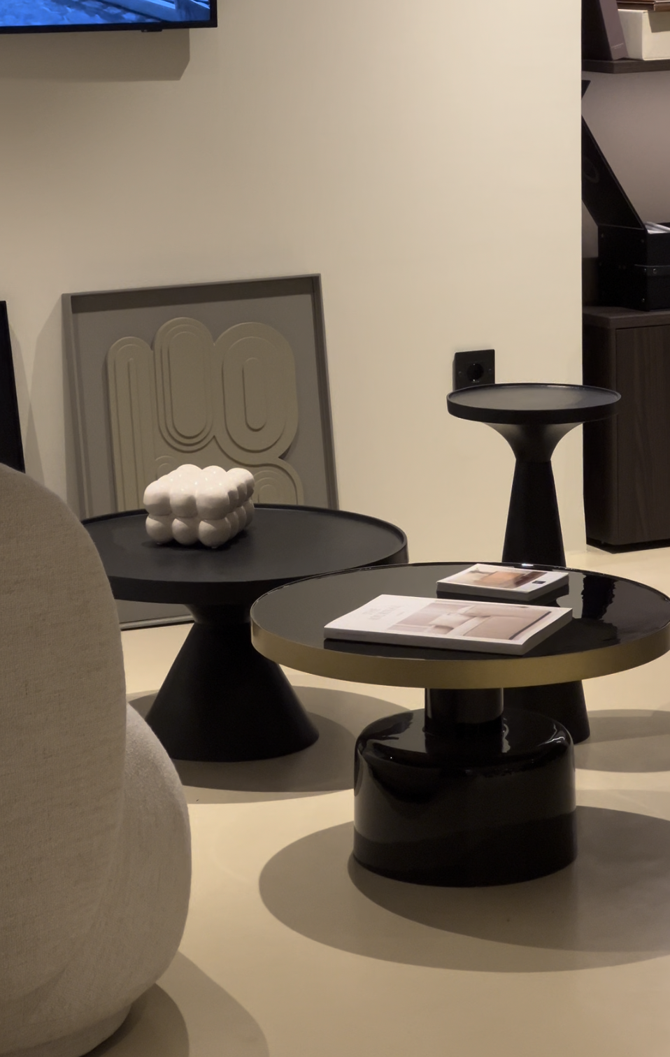 Deux tables d'appoint noires avec des magazines dessus, une décoration blanche en forme de nuage et une œuvre d'art abstraite derrière, dans un intérieur contemporain.