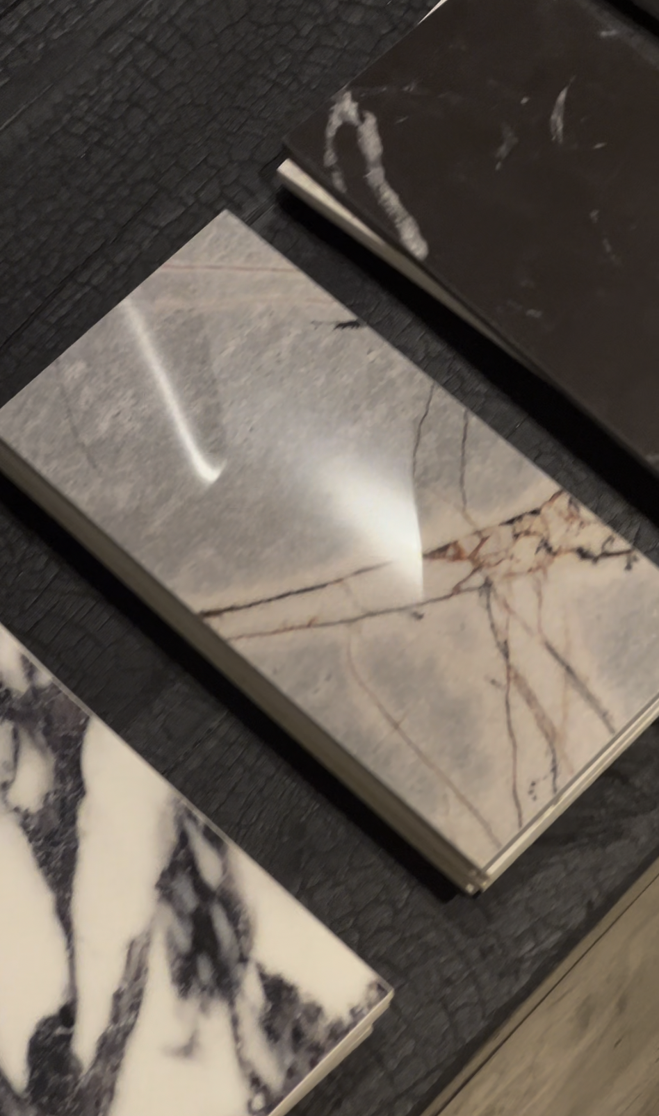 Échantillons de carreaux de pierre naturelle avec différentes textures et couleurs, dont gris uni, beige avec veines roses et noir et blanc marbré.