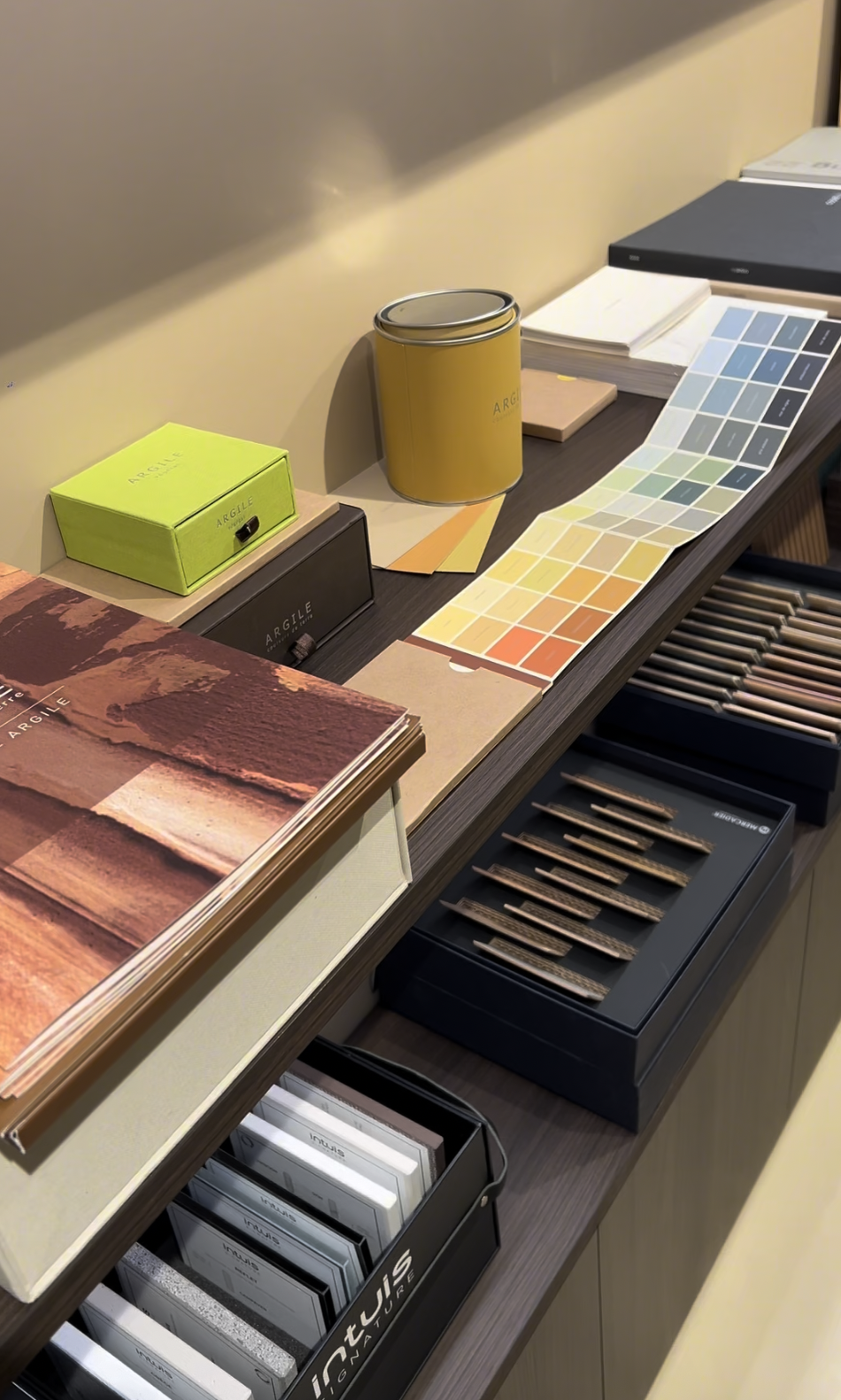 Échantillons de peinture, cartes de couleurs, brochures, et boîtes de rangement sur un comptoir, probablement dans un magasin de décoration ou de peinture.