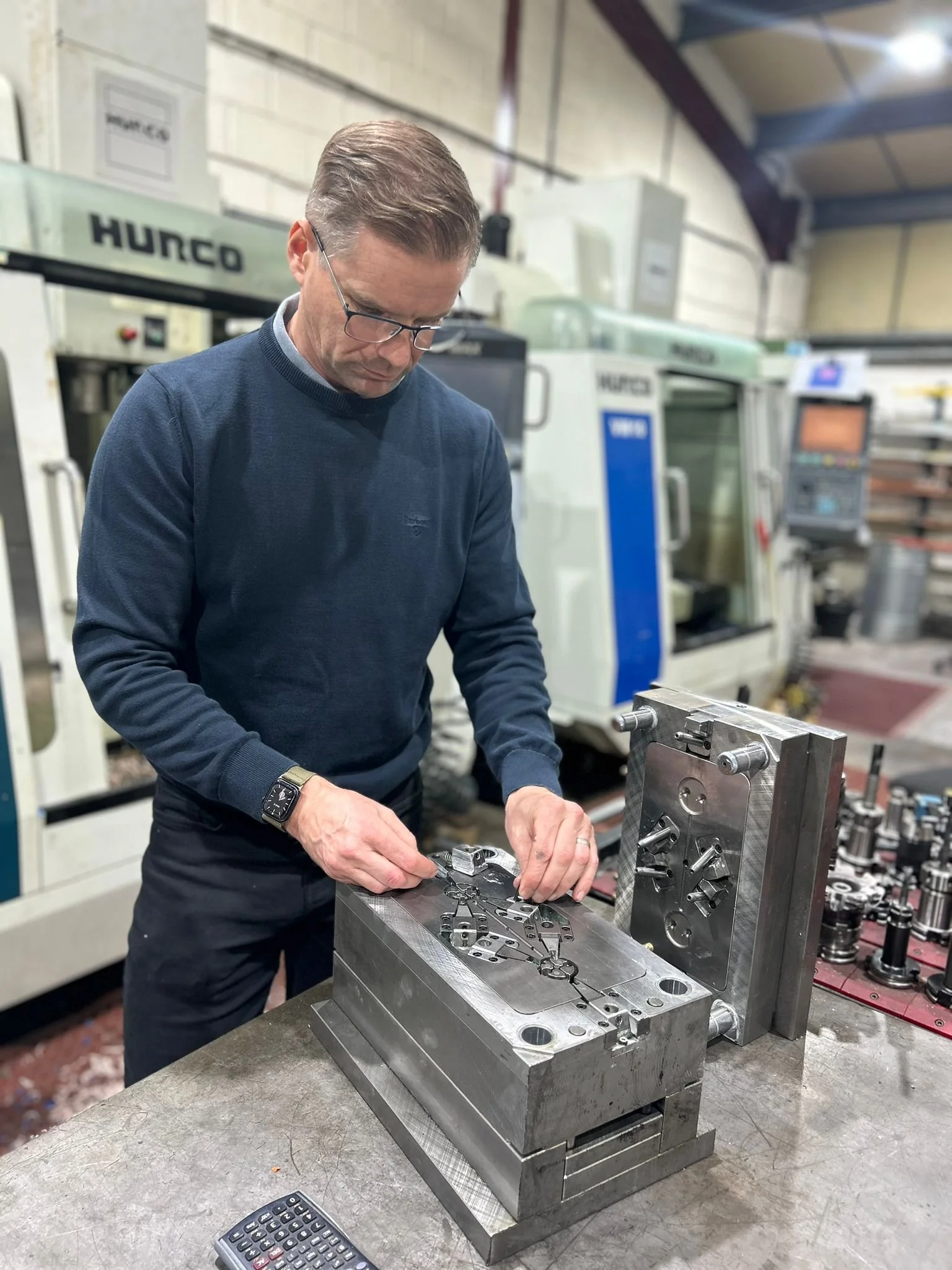 A man working with metal parts on a machine in a manufacturing workshop.
