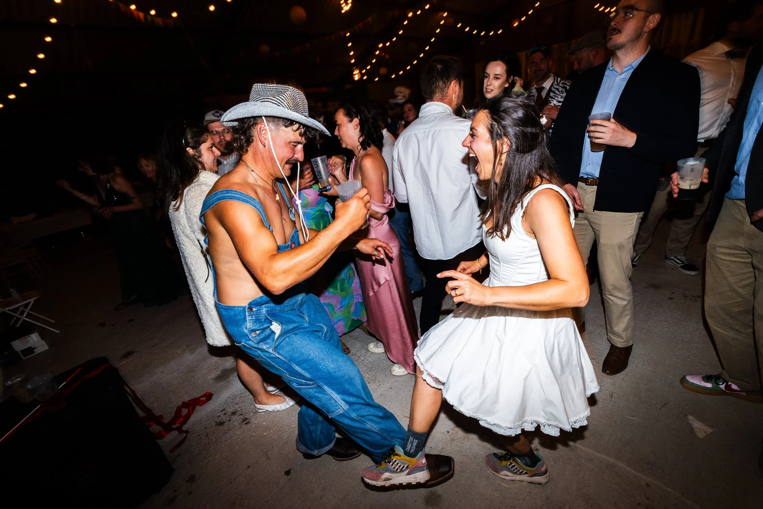 People dancing and having fun at a party or celebration with string lights overhead.