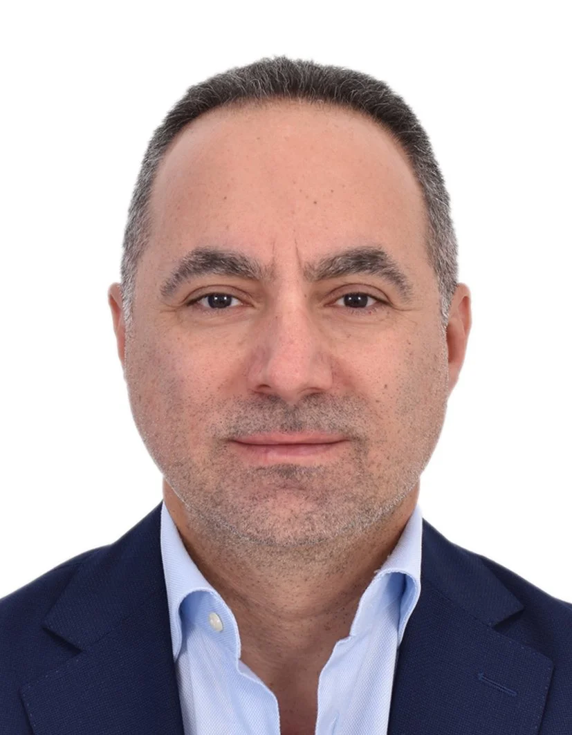 Wissam Najjar: a middle-aged man with short dark hair, wearing a navy blazer and light blue dress shirt, against a plain white background.