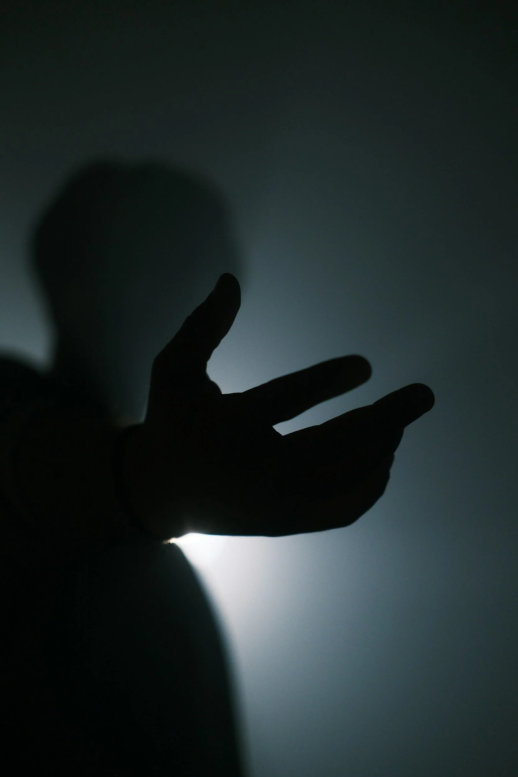 Silhouette of a person making a peace sign with their fingers, backlit with a glow behind them, creating a shadow effect.
