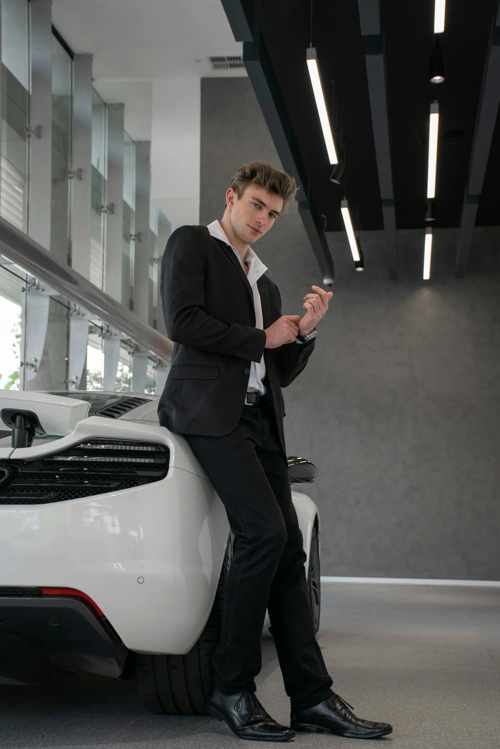 Man in a suit standing beside a vehicle in a modern car dealership, representing a private one-on-one consultation for automotive sales, body language, and persuasion training.