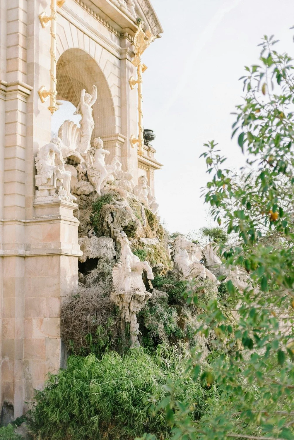 Exterior view of a building with elaborate sculptures, including human figures, nestled among greenery and rocks.
