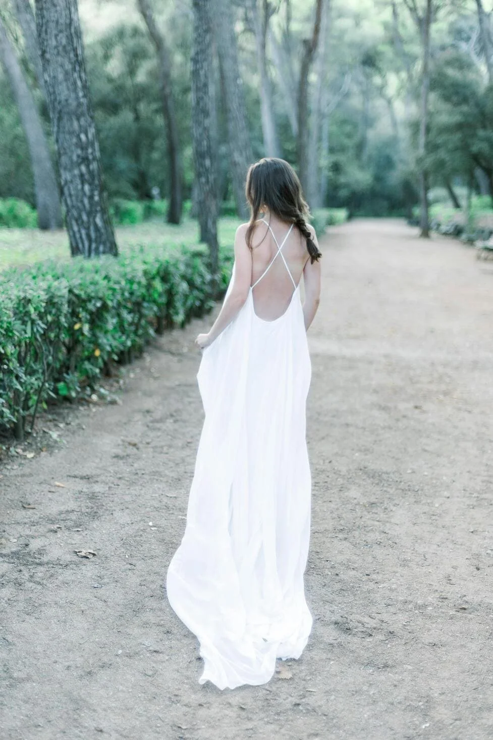 Woman in a white dress walking on a dirt path in a wooded park.