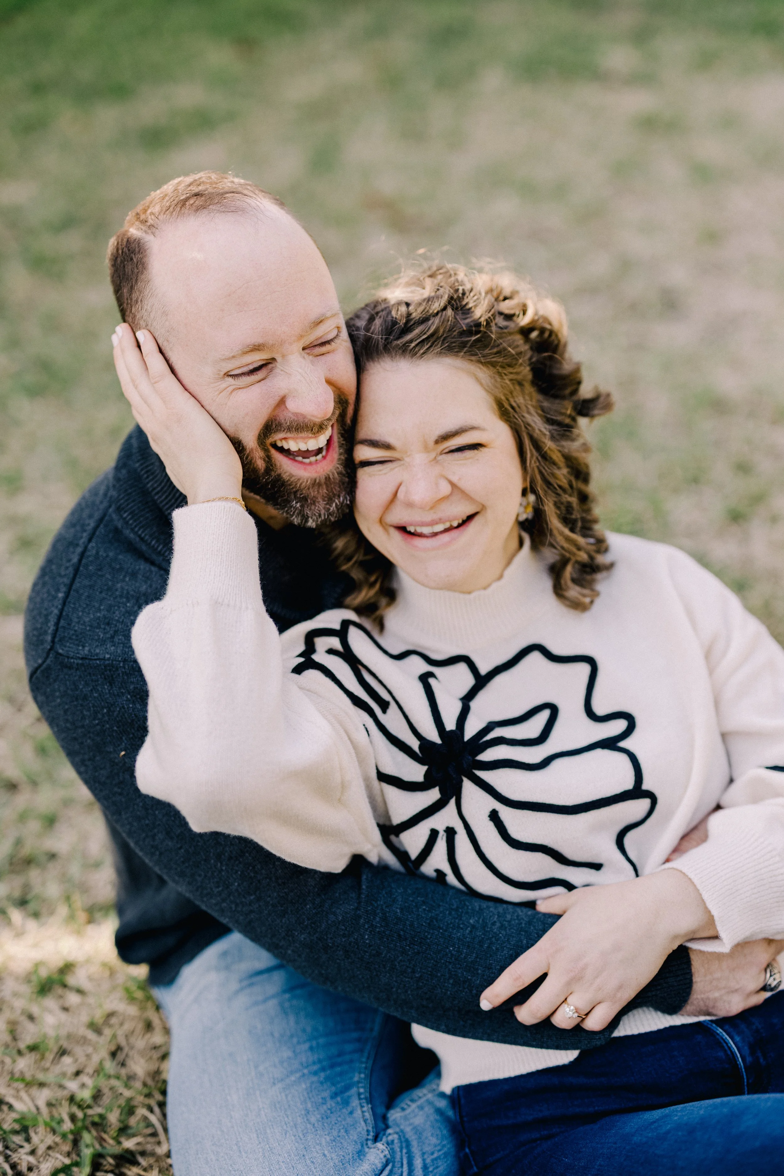 A joyful couple sitting outdoors, hugging and laughing together.