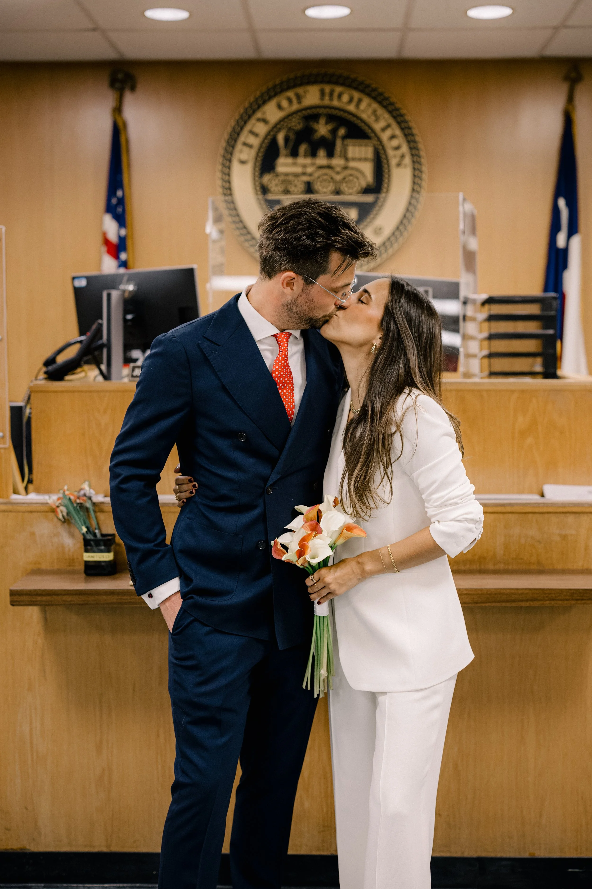 A newly married couple sharing a kiss in a courthouse, with the bride holding a bouquet of calla lilies.